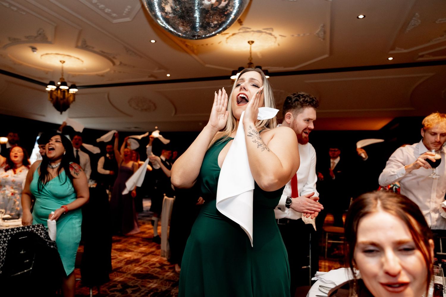 Guests celebrating at a wedding reception on a dance floor beneath a disco ball in an elegant venue.