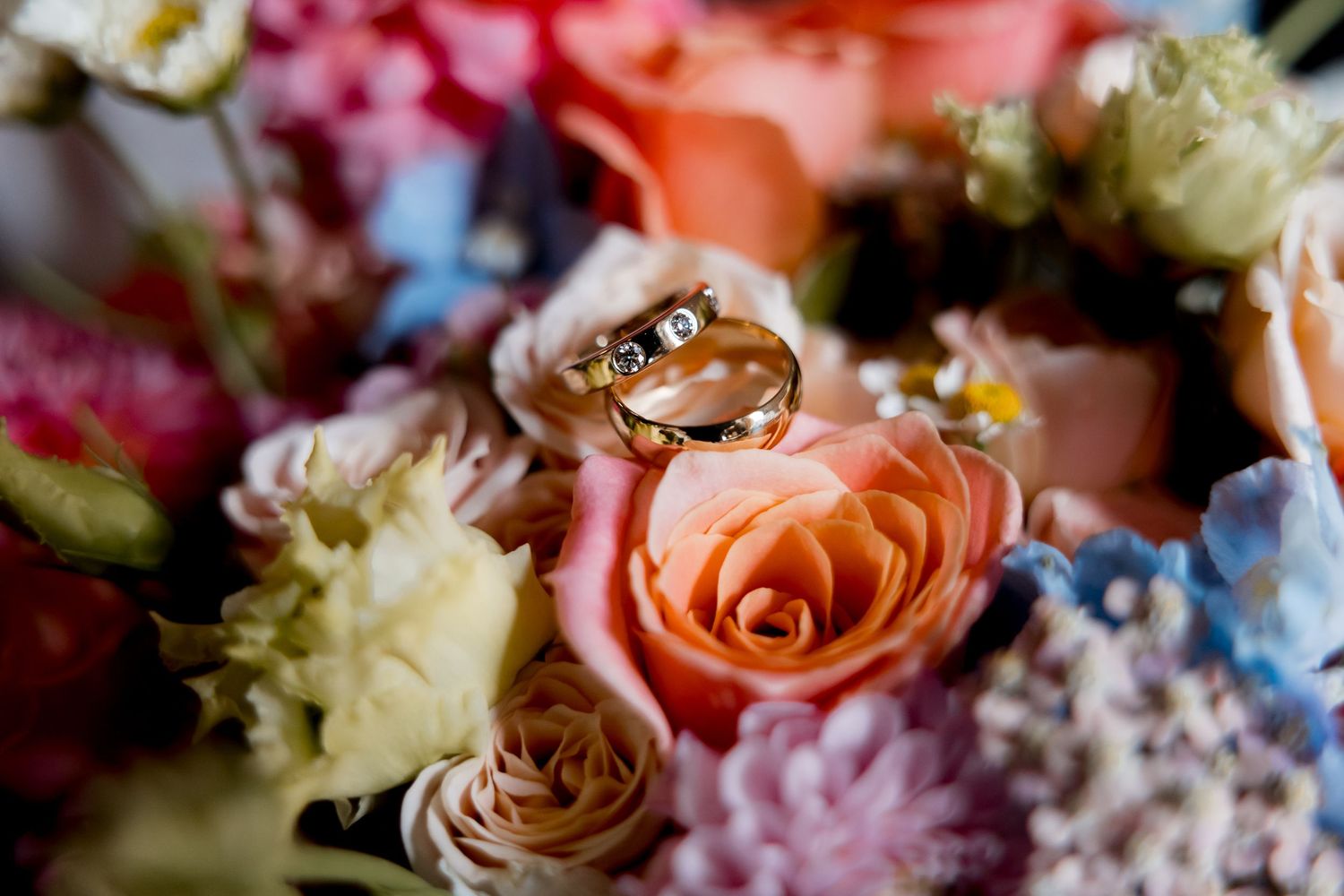 Delicate floral arrangements featuring coral roses and pastel blooms with wedding rings nestled among the petals.