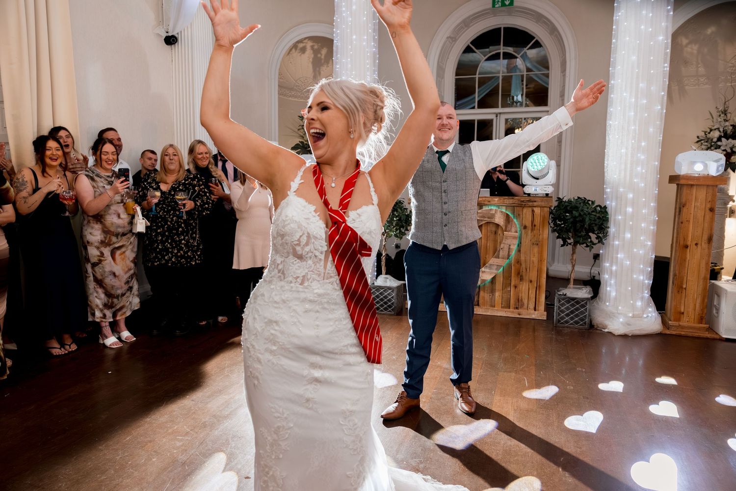 Wedding reception dance floor filled with joyful guests celebrating with raised arms.