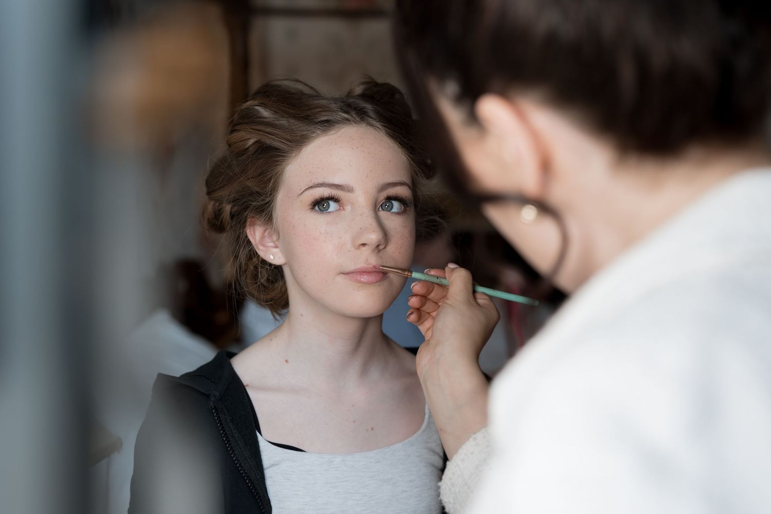 Final touches of bridal makeup being applied in soft natural light.