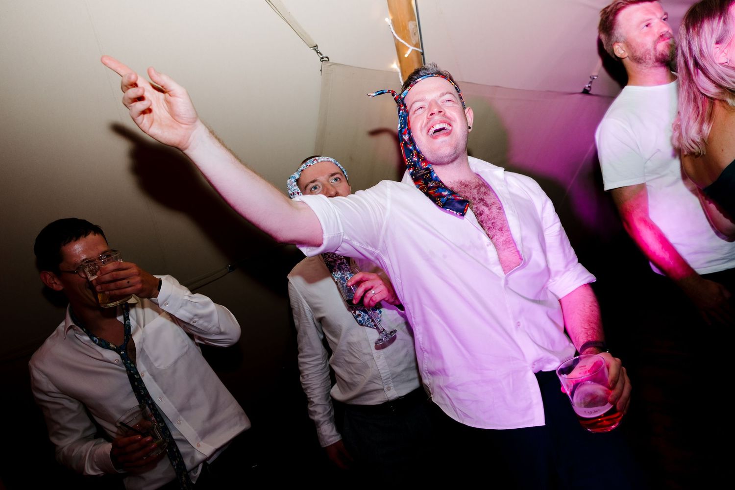 Wedding guests dancing and celebrating on a lively dance floor with pink lighting.
