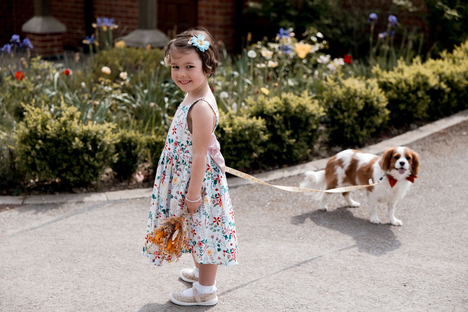 Wedding guests walking through sunny garden path in summer dresses.