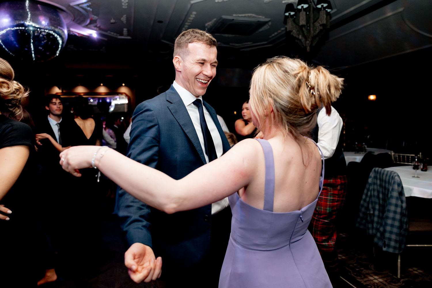 Couple dancing joyfully at wedding reception in dimly lit venue.