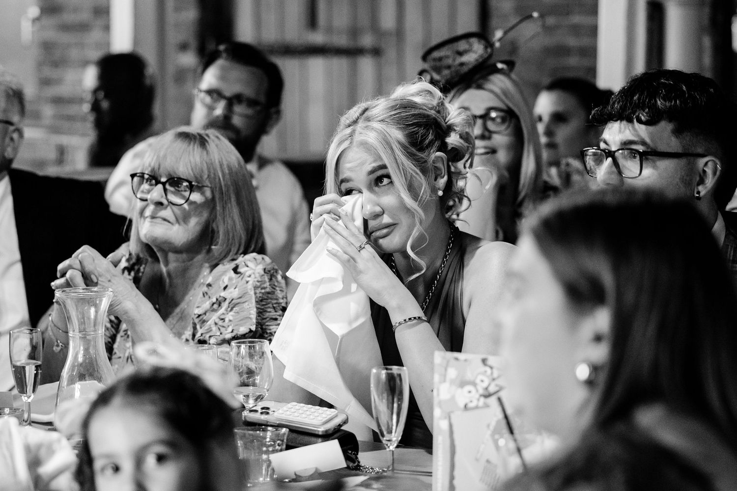 Black and white candid shot of emotional wedding reception reactions during speeches.