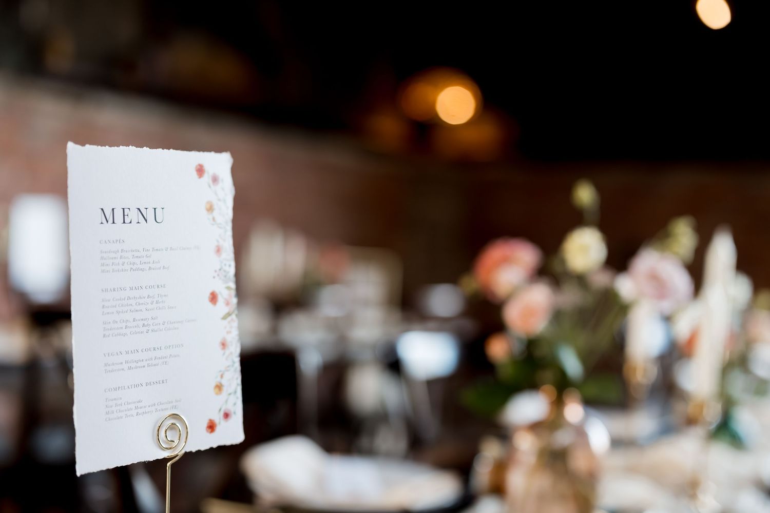 Wedding menu card displayed at decorated reception table with soft focus background.
