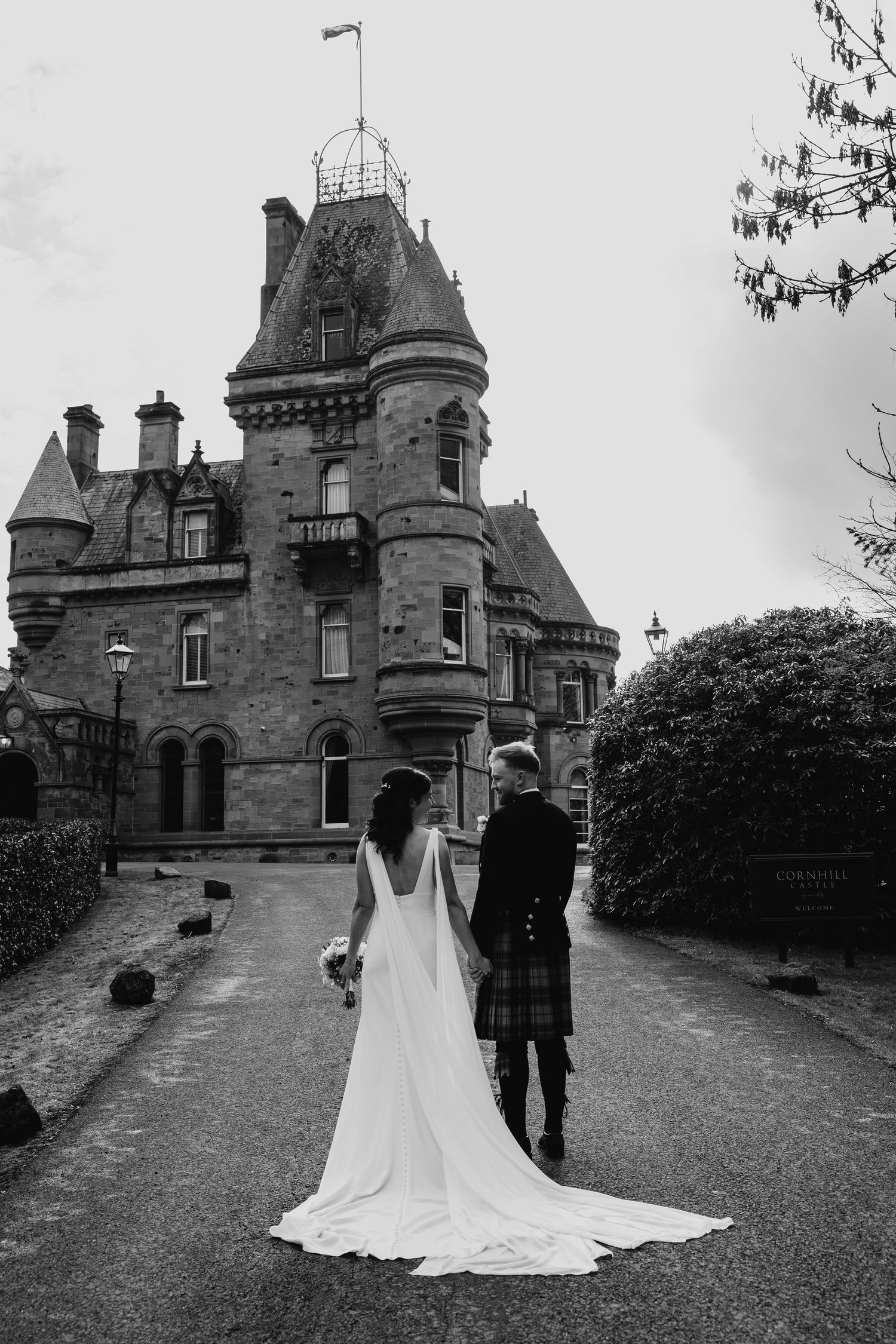 Black and white photo of bride and groom walking toward a grand Scottish castle venue.