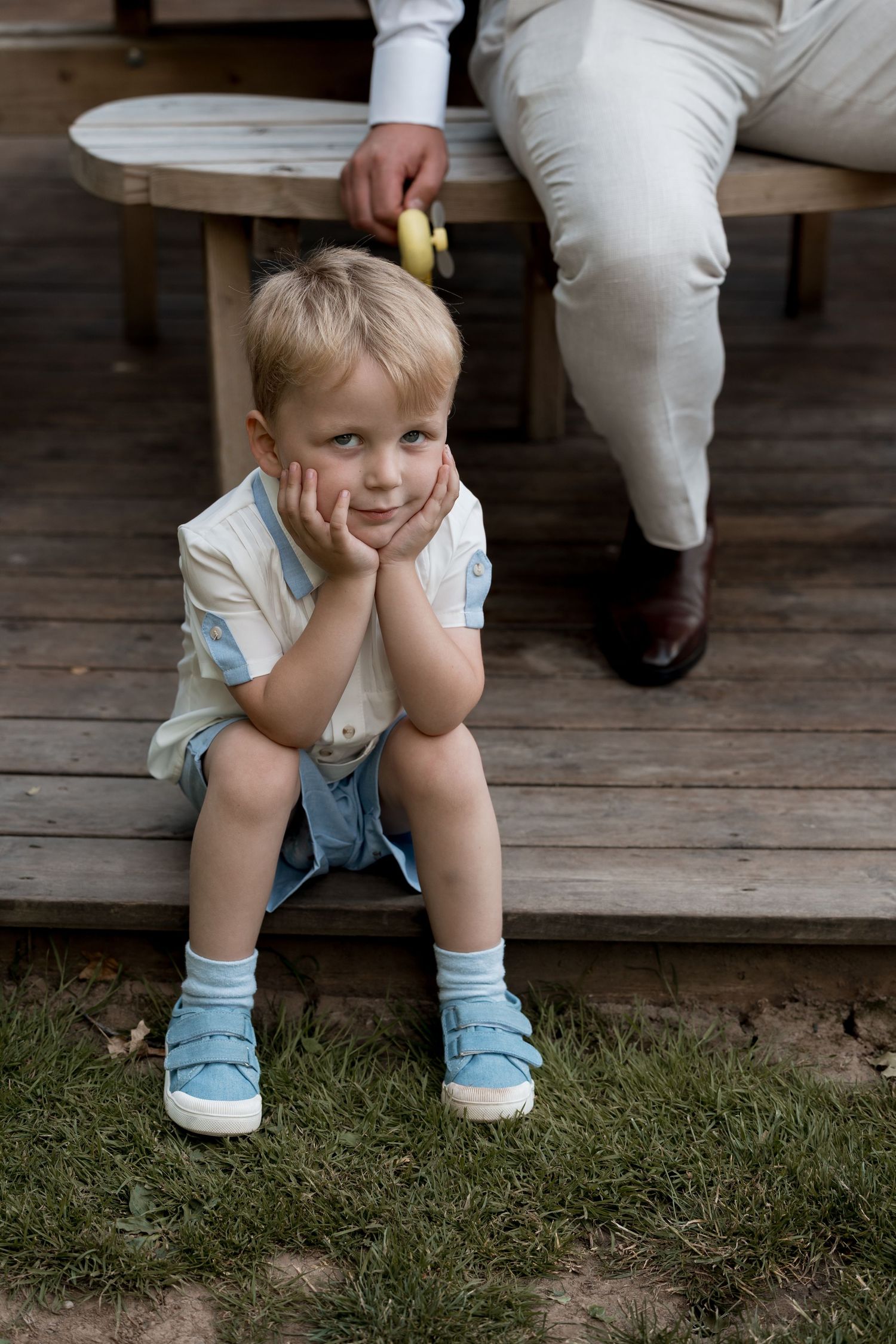 Small child in blue socks sits on wooden steps during a wedding.