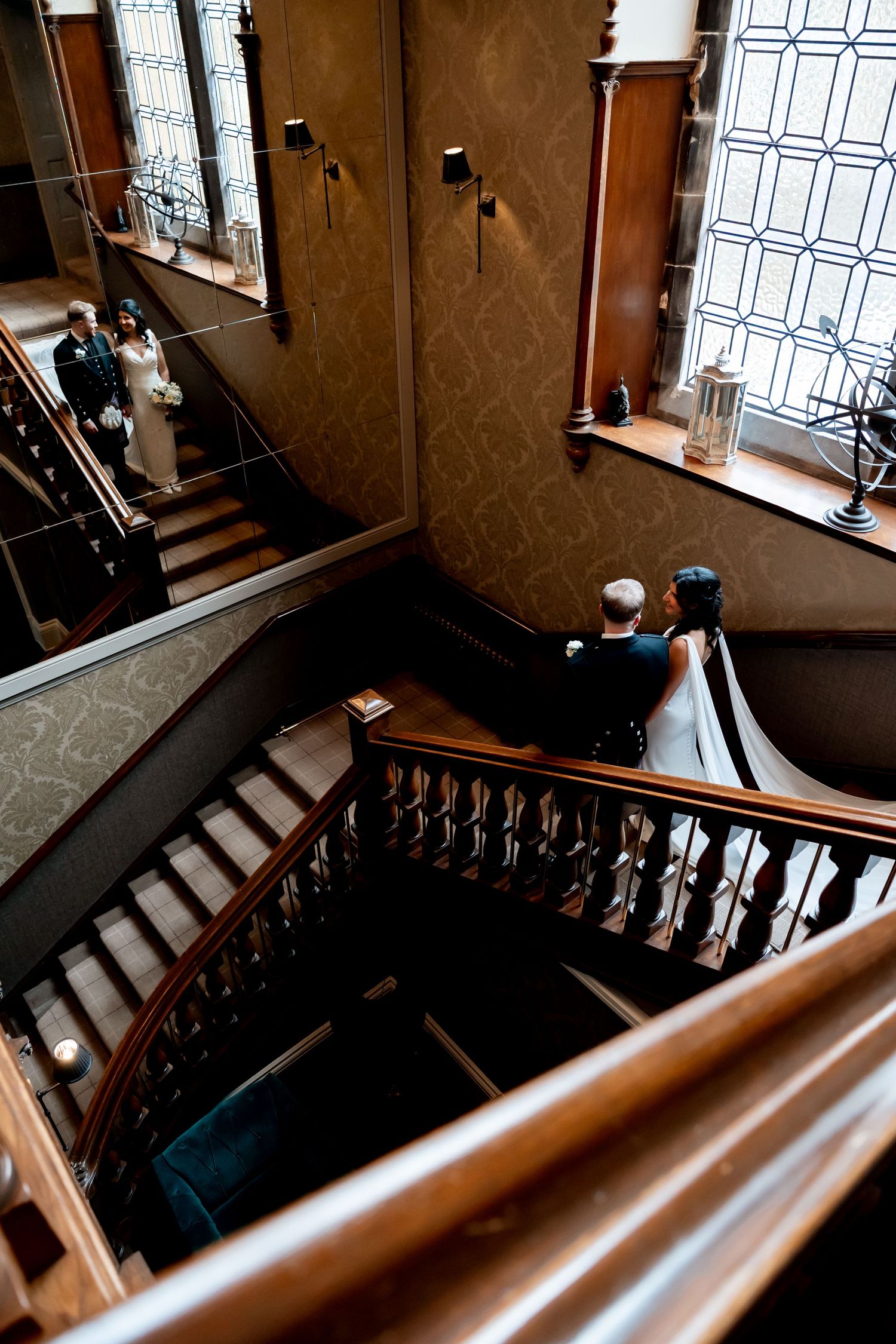 Aerial view of bride and groom descending an elegant wooden staircase in a historic venue.