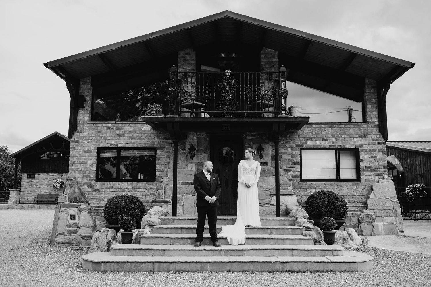 Black and white photo of a couple standing outside a rustic stone building with decorative balconies.
