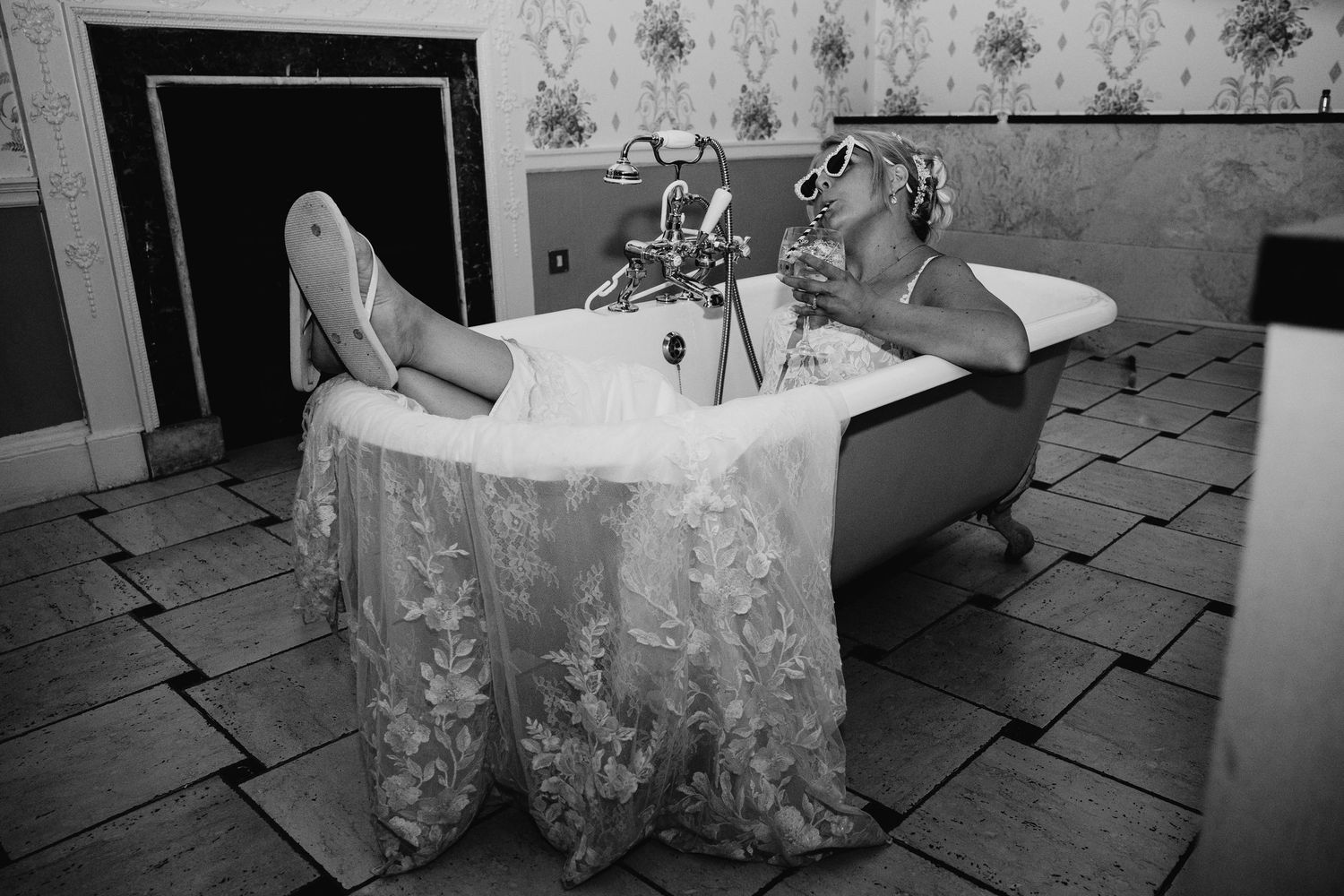 A black and white photo of a bride relaxing in a vintage clawfoot bathtub.