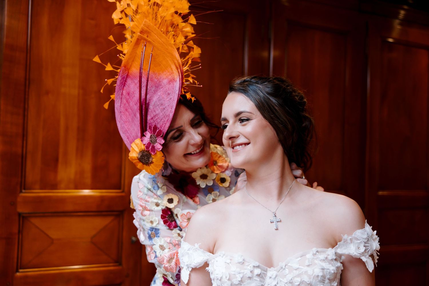 Two wedding guests share a joyful moment against a wooden paneled wall with dramatic orange lighting.