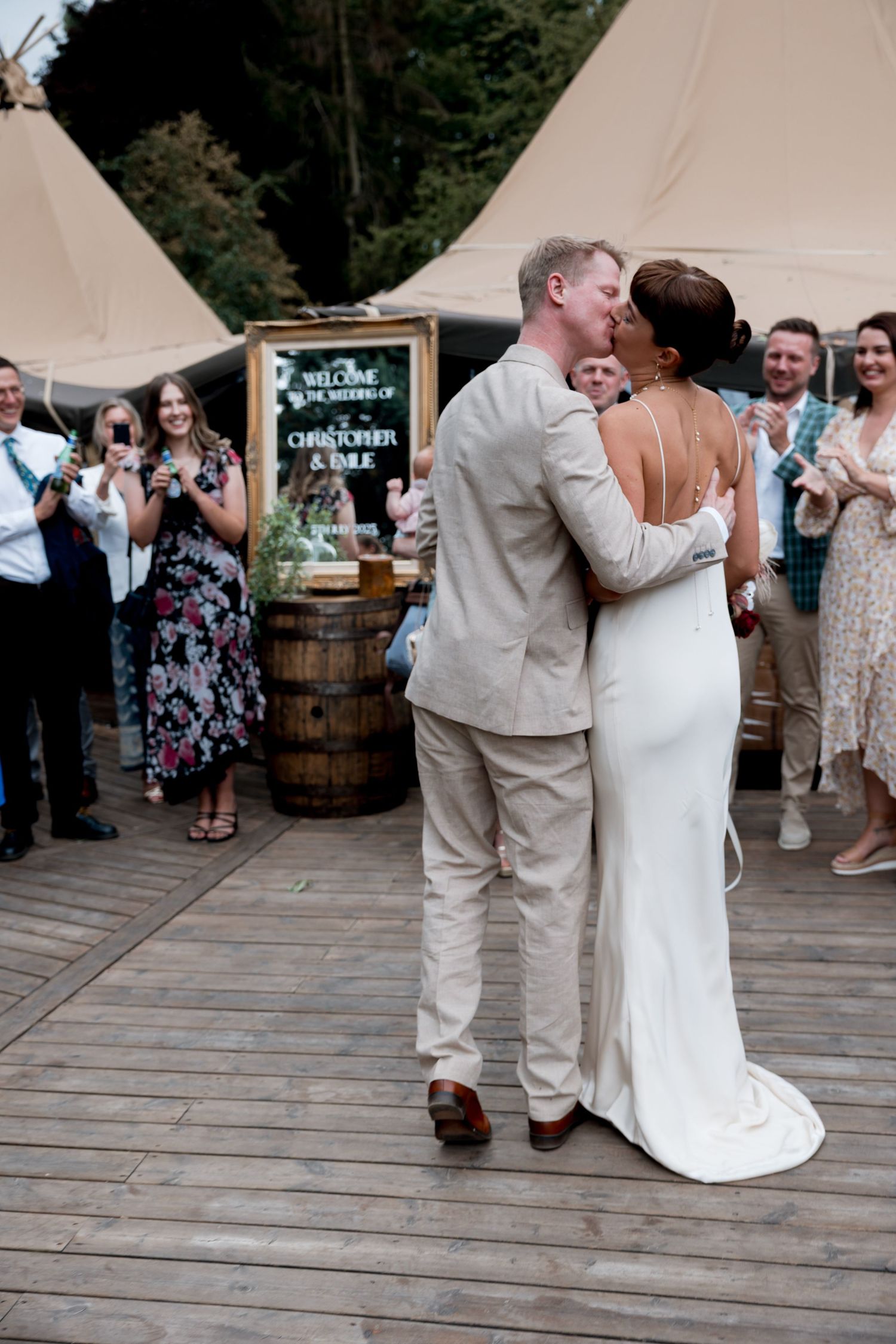 Wedding couple dancing on wooden deck surrounded by guests and rustic decor.