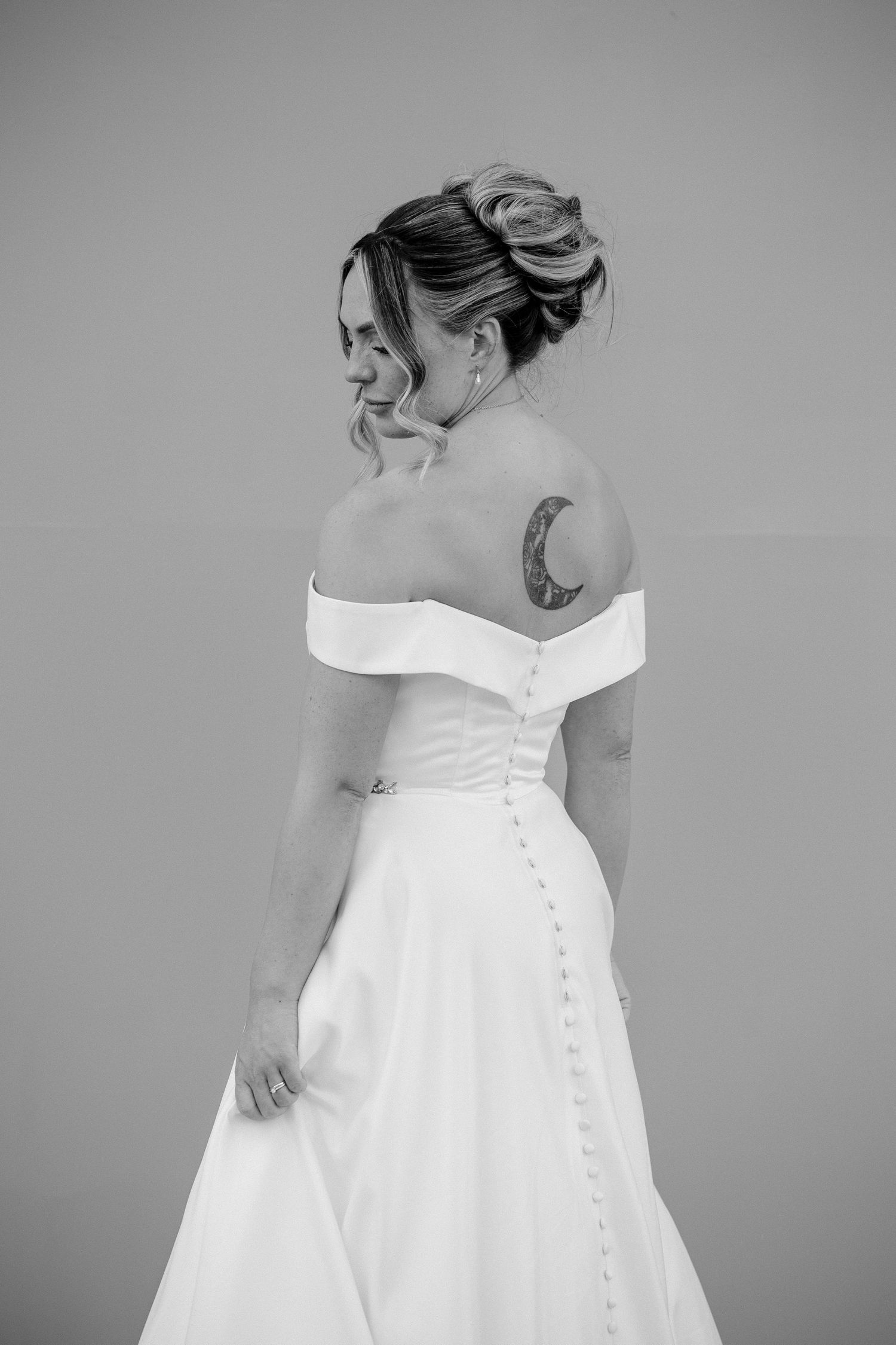 Black and white photos showing details of an elegant off-shoulder wedding dress with button closures and gathered fabric.