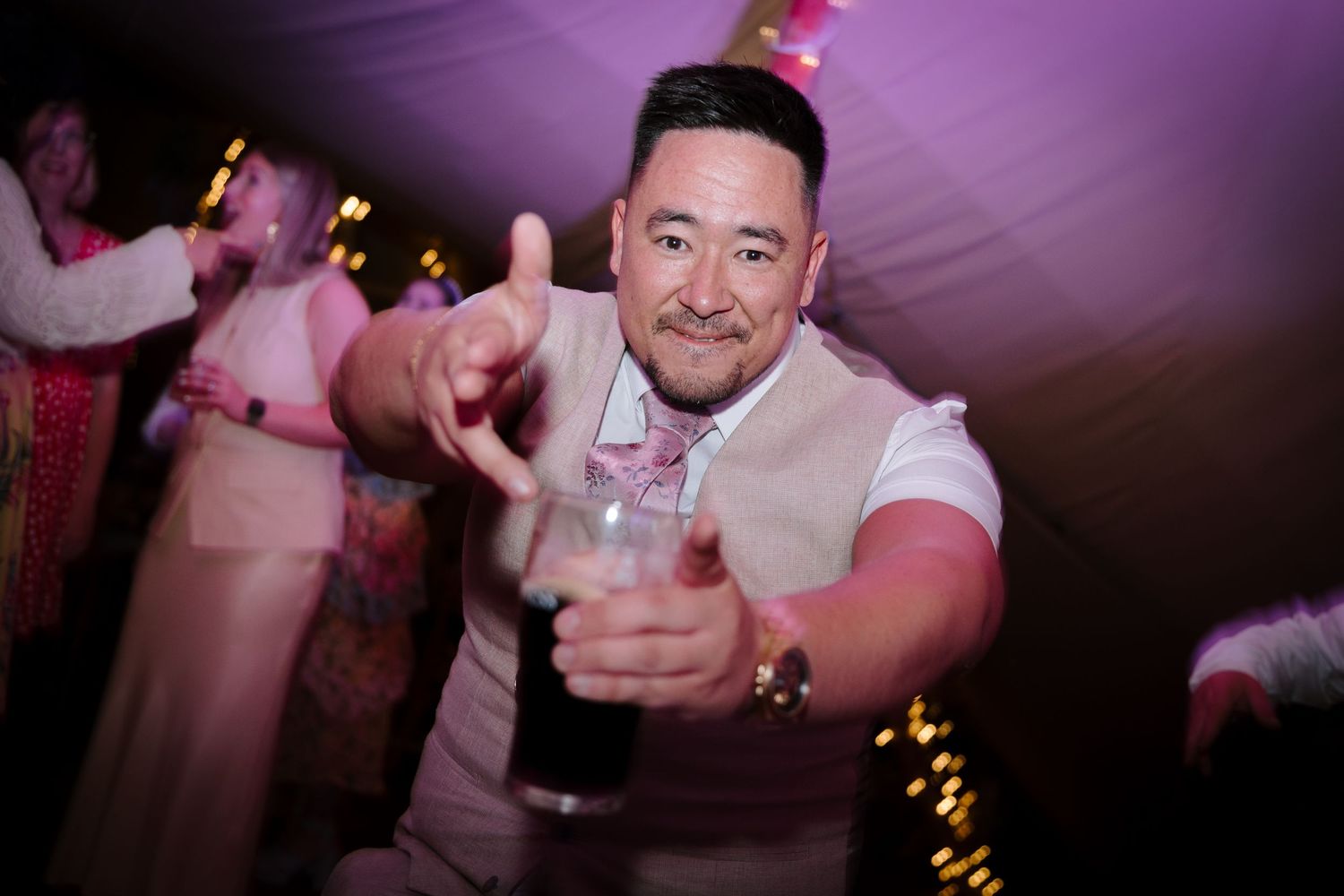 Party guests dancing and celebrating under purple mood lighting.