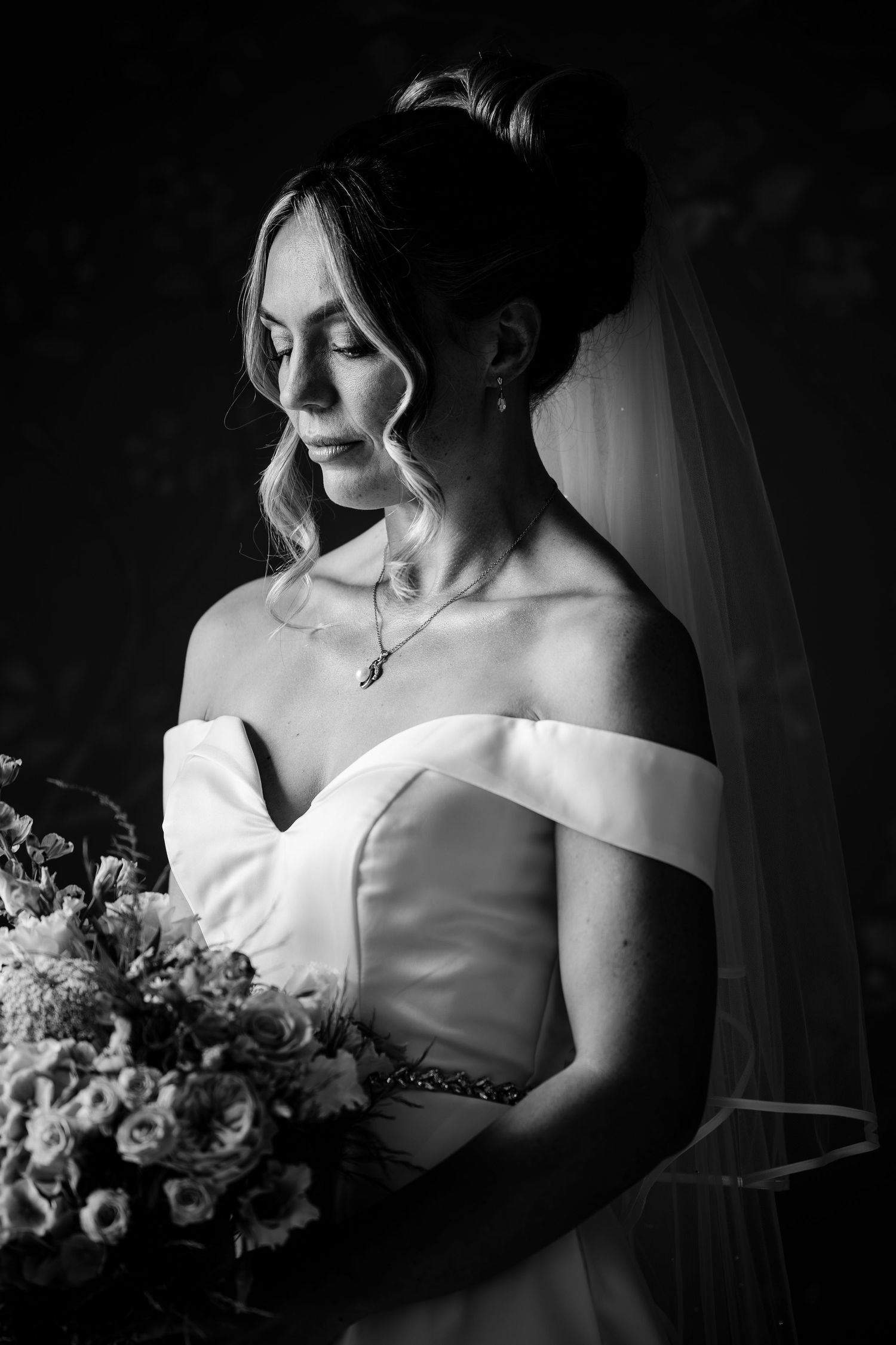 Dramatic black and white portraits of bride in off-shoulder wedding dress holding bouquet.