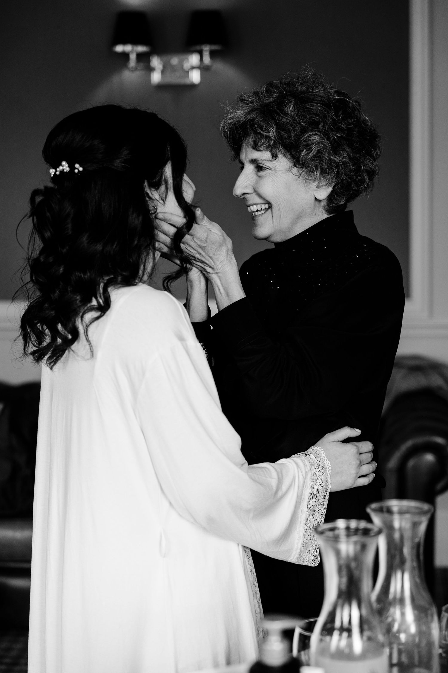Black and white photo of a bride and older woman sharing a joyful moment during wedding preparations.