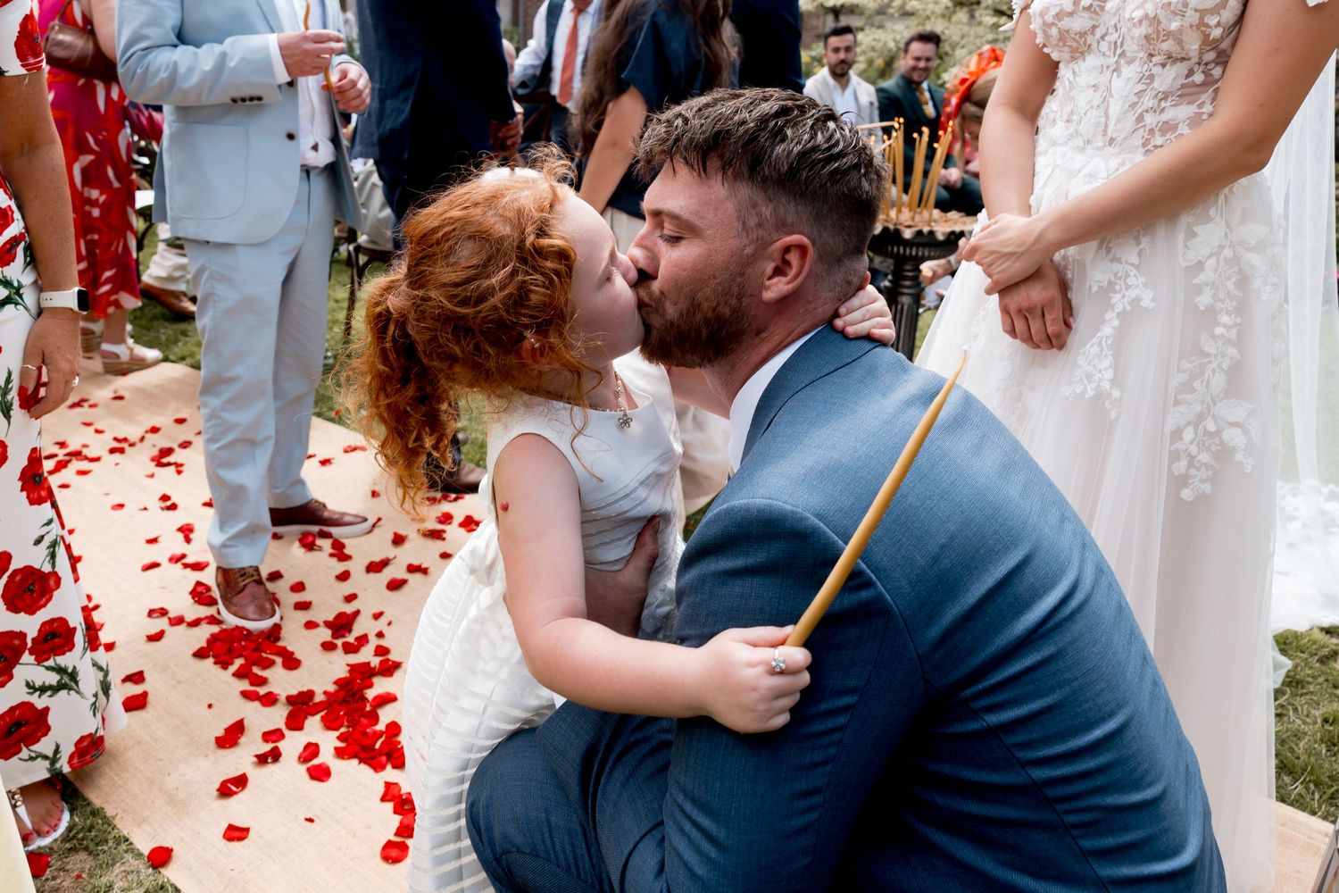 Sweet moment at outdoor wedding ceremony with red rose petals scattered on the ground.