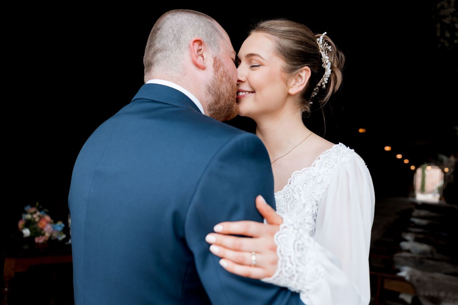 Romantic wedding couple embracing in formal attire against dark background.