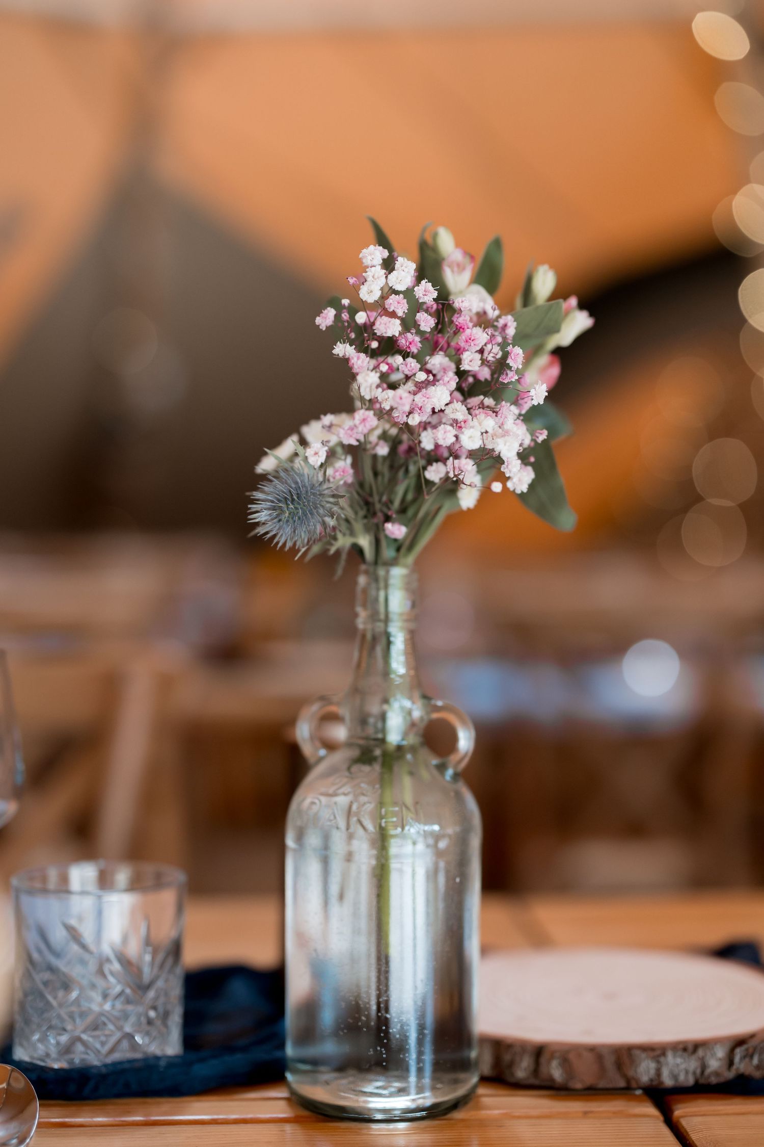 Delicate floral centerpieces in glass jars arranged on wooden table settings.