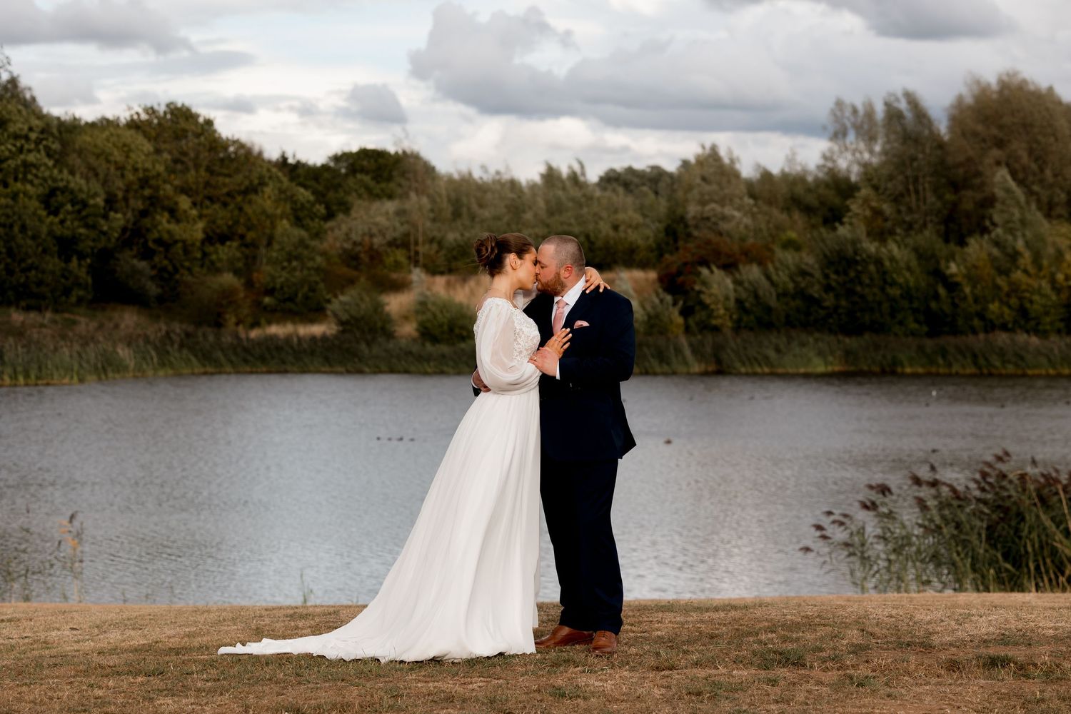 A lakeside wedding portrait session with dramatic cloudy skies in the background.