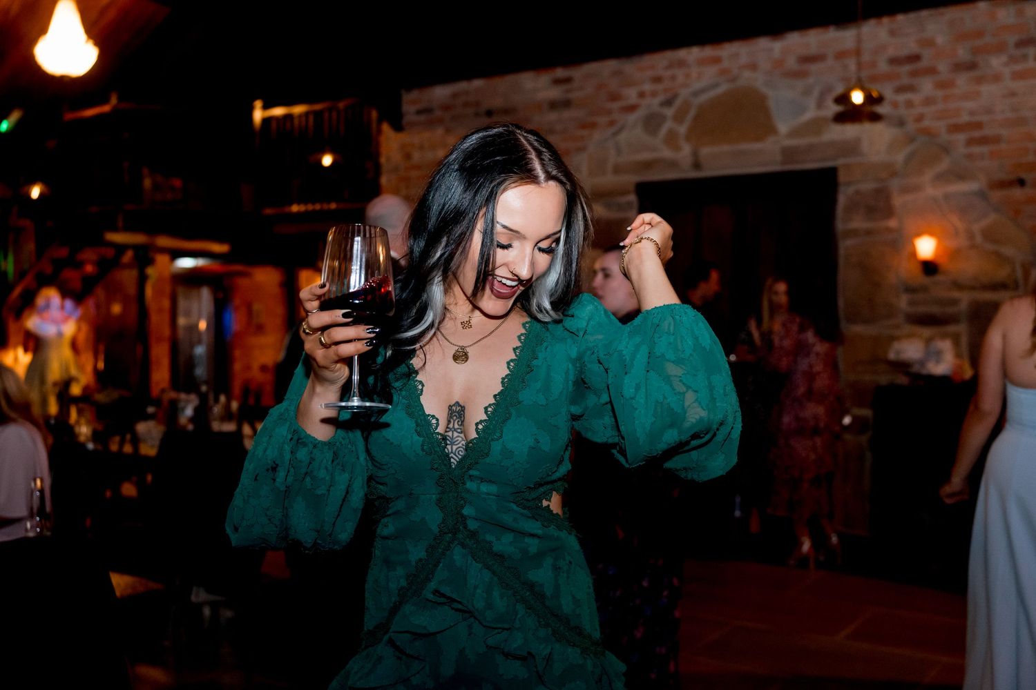 Woman in emerald green dress dancing at dimly lit party venue.