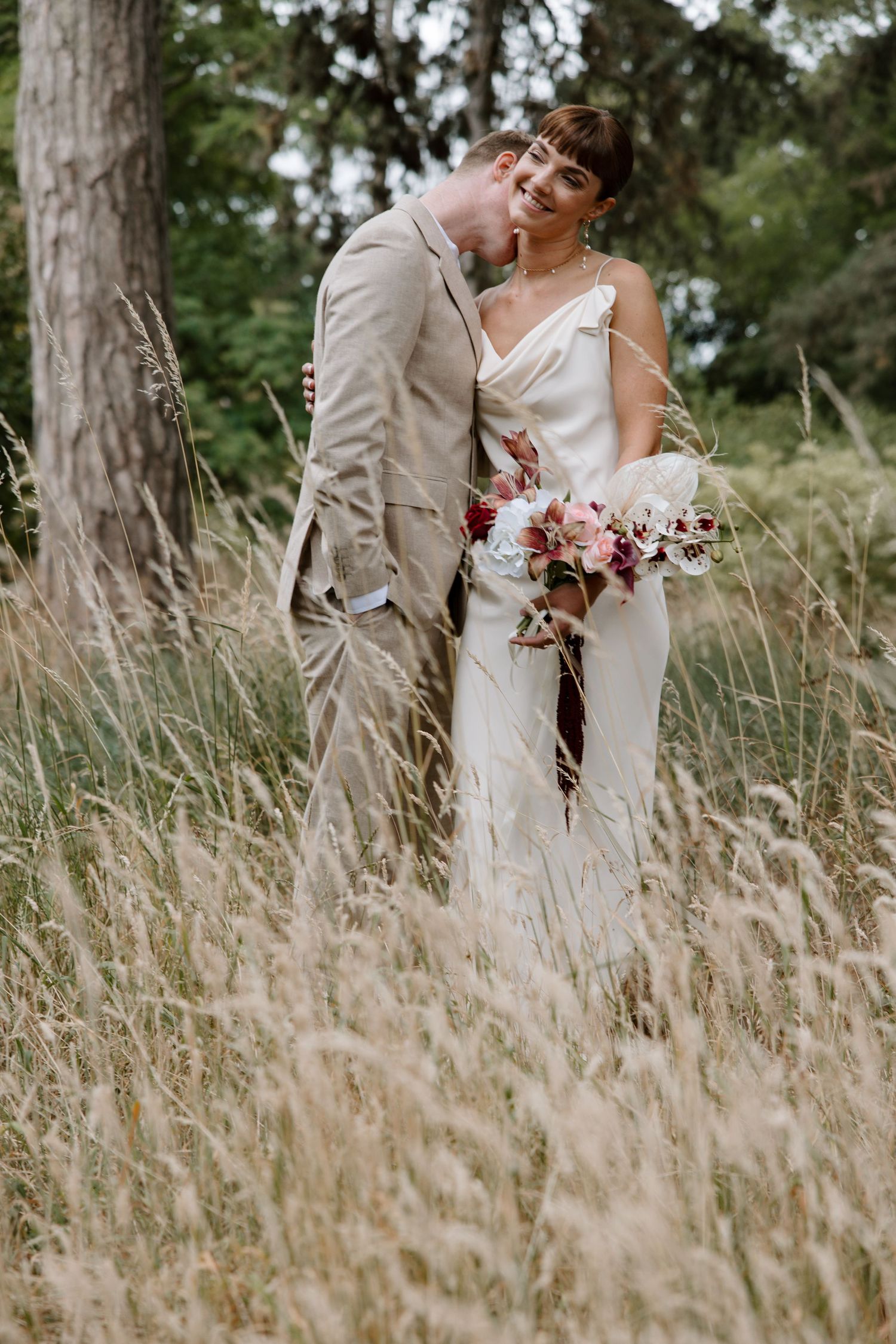 Newlyweds sharing intimate moment in tall grass field.