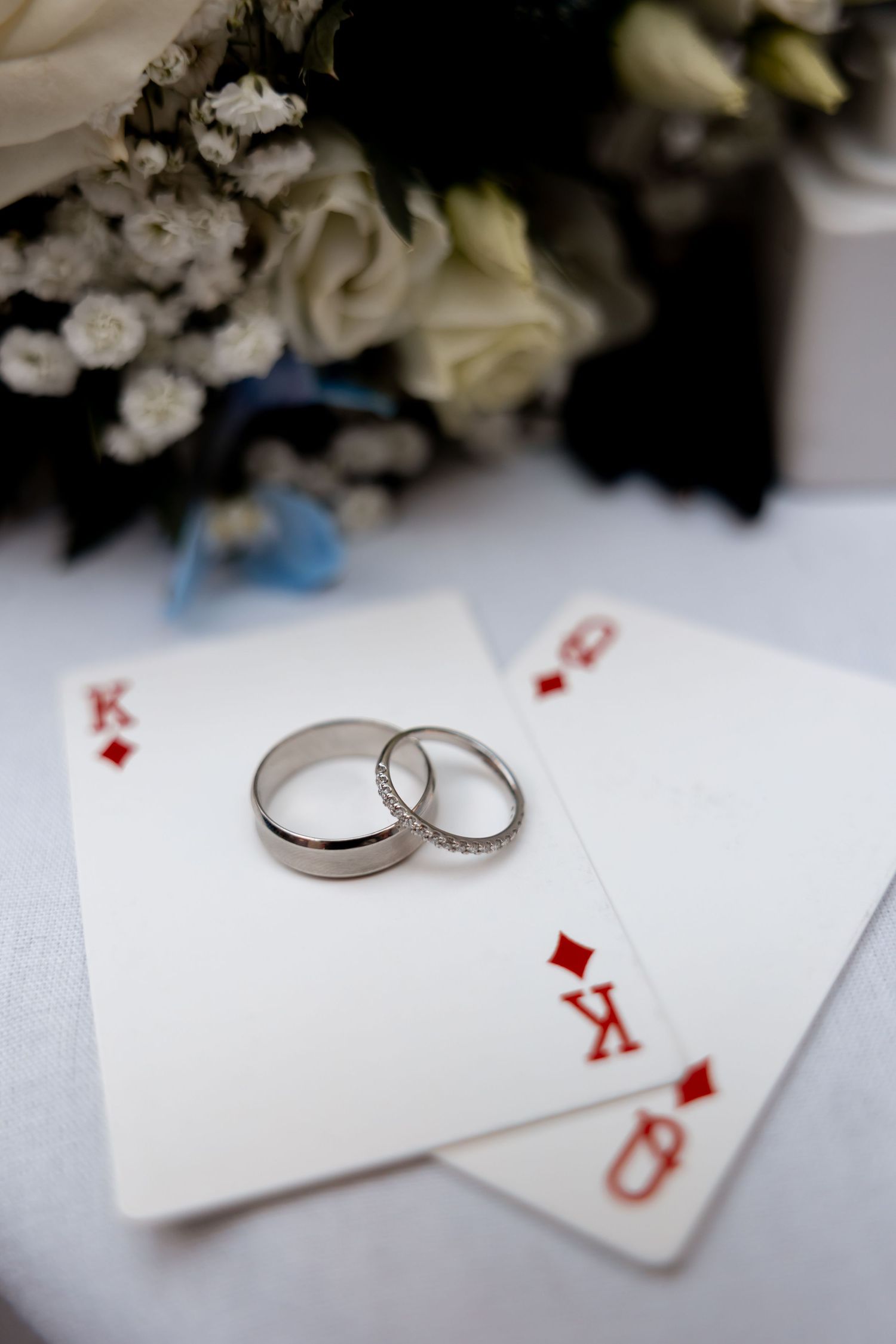 Two wedding bands resting on King and Queen of diamonds playing cards with white roses bouquet.