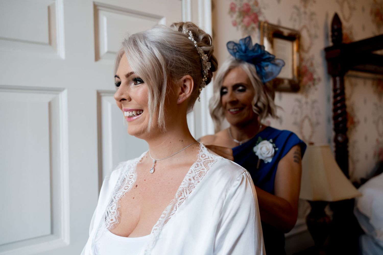 Bride getting ready in white robe against vintage floral wallpaper background.
