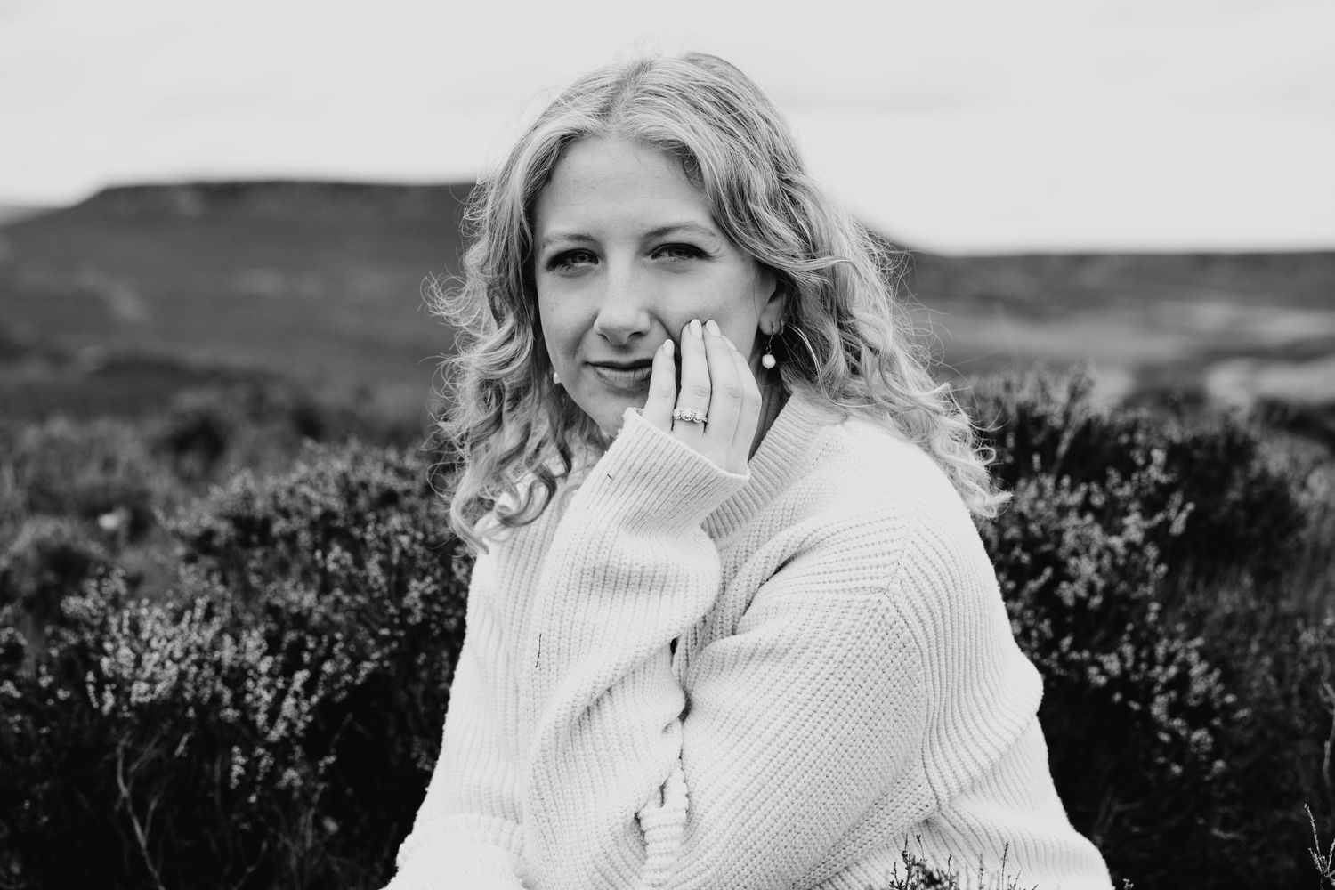 A candid black and white portrait of someone laughing against a rural landscape background.