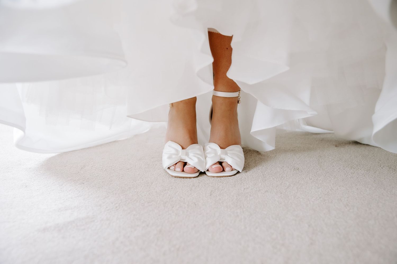 A close-up view of white bridal shoes on a light background with elegant styling details.