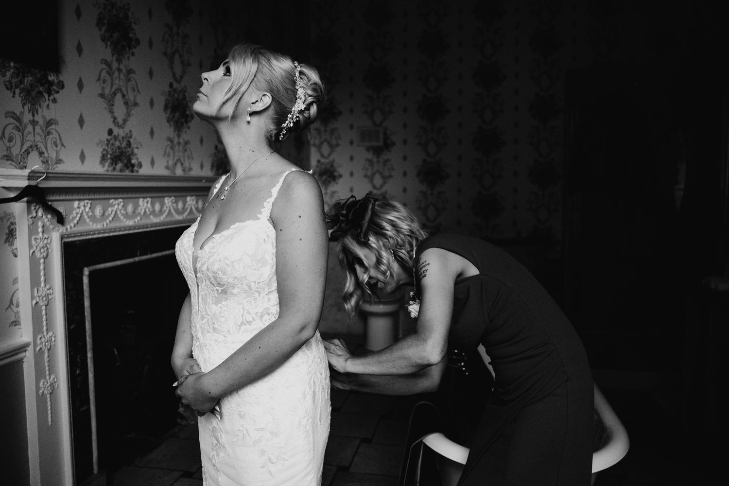 Black and white photo of a bride in a white dress getting final adjustments to her gown before the ceremony.