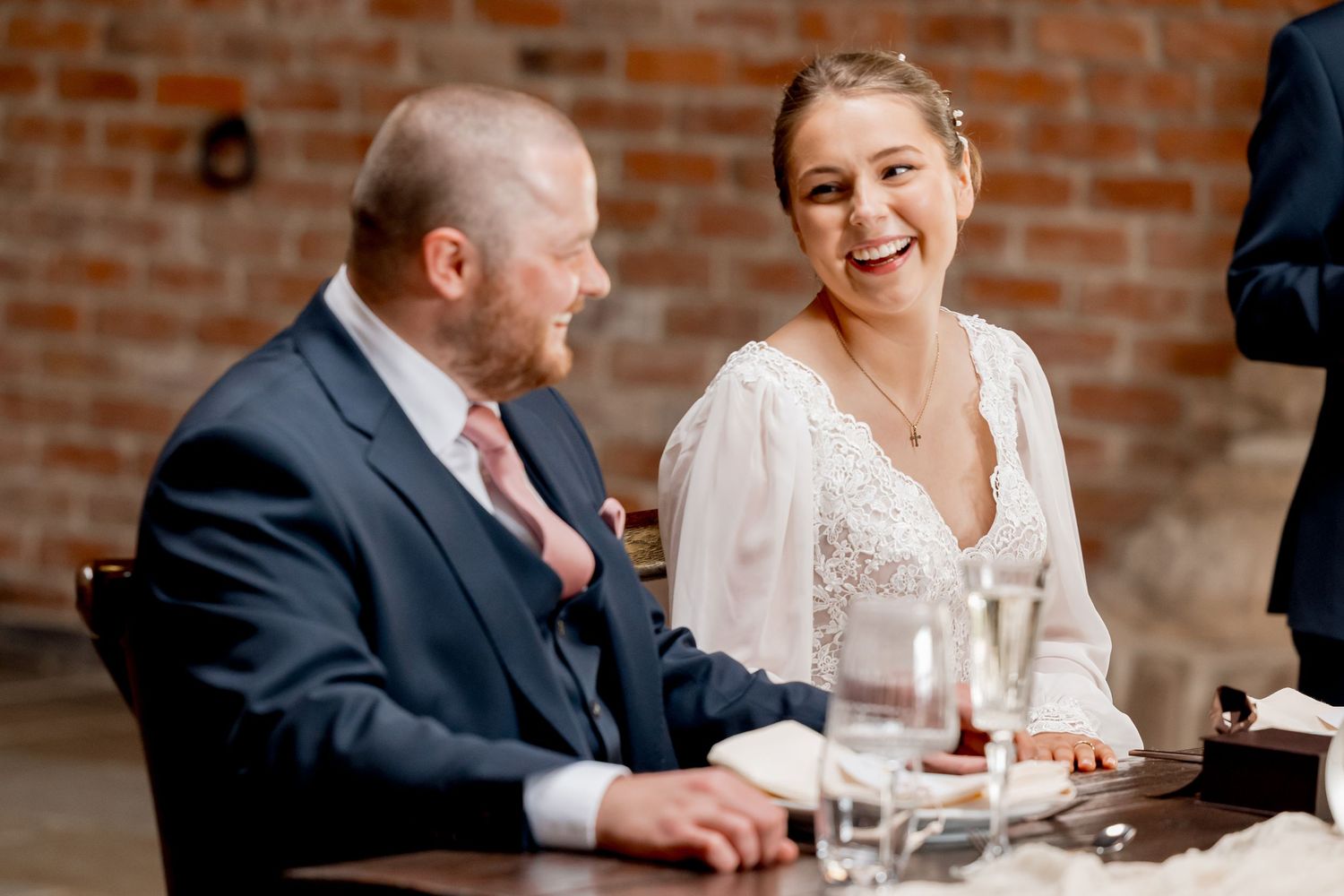 Newlyweds share a meal together at their reception with exposed brick walls.