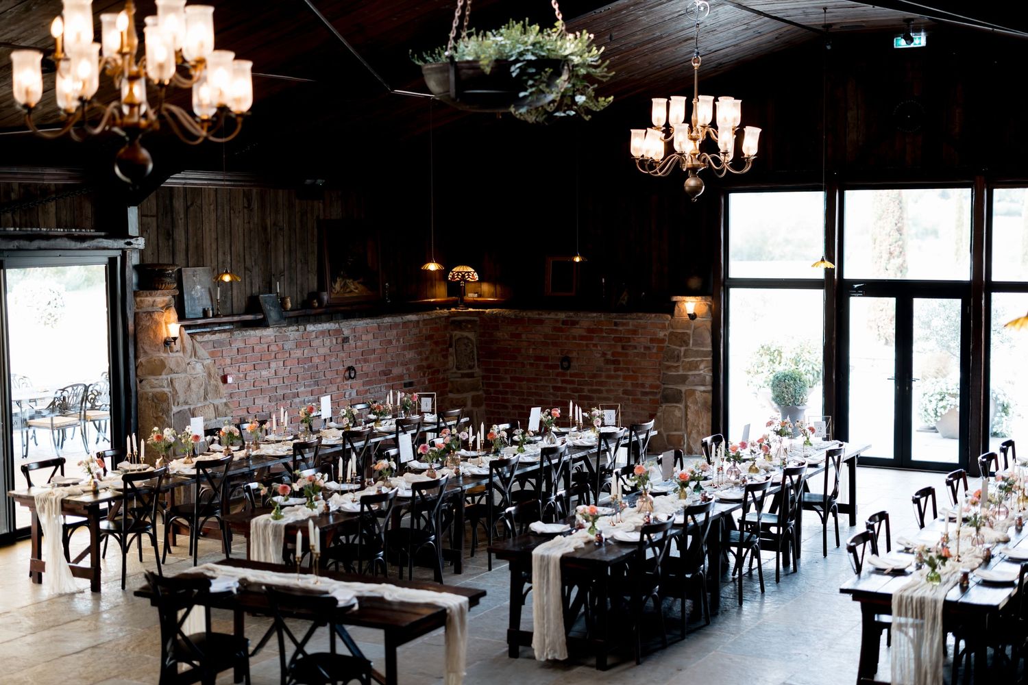 Rustic wedding reception venue with elegant chandeliers and table settings in a barn-style space.