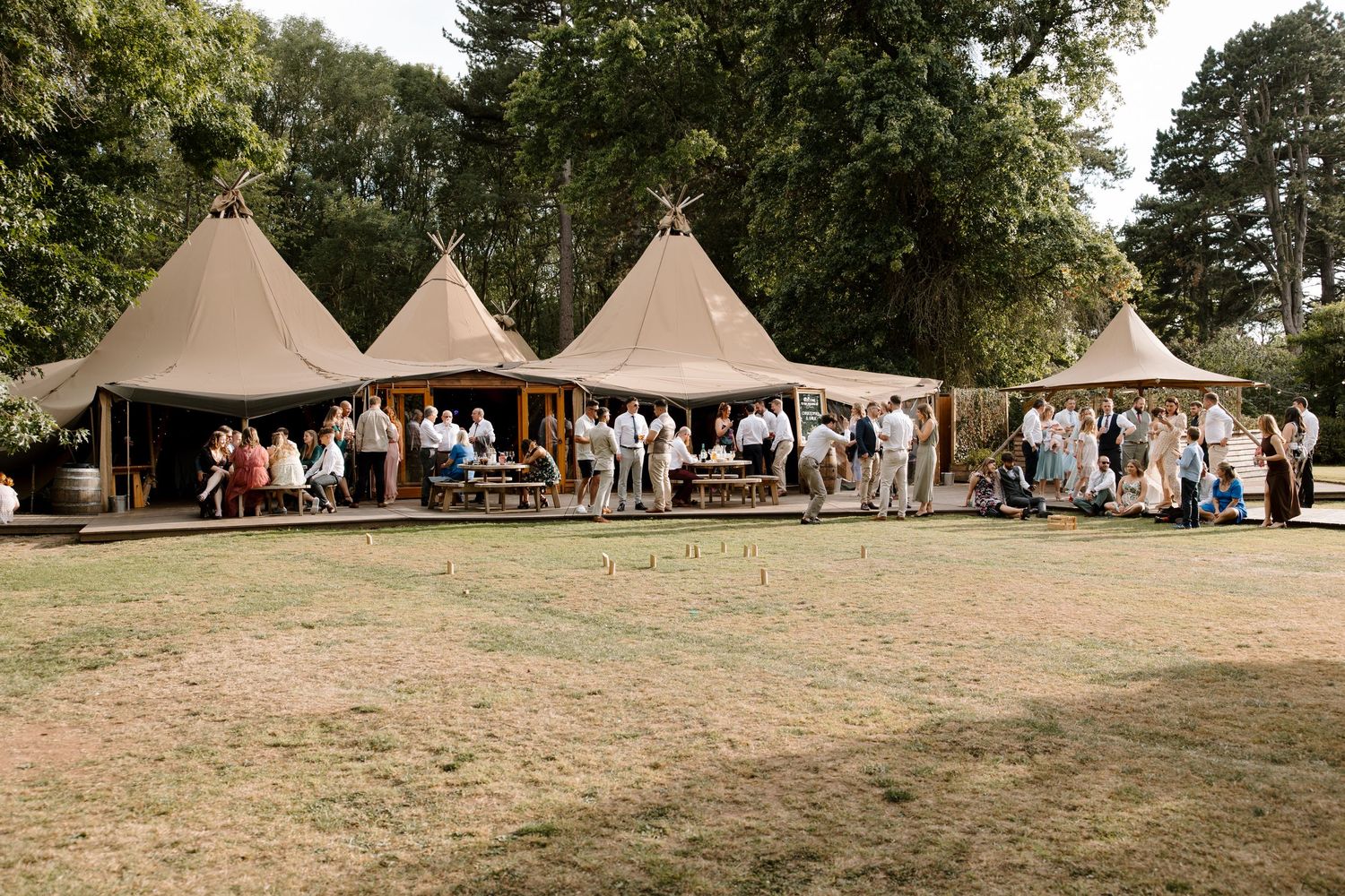 Multiple tipi tents arranged in a field surrounded by trees for an outdoor event.