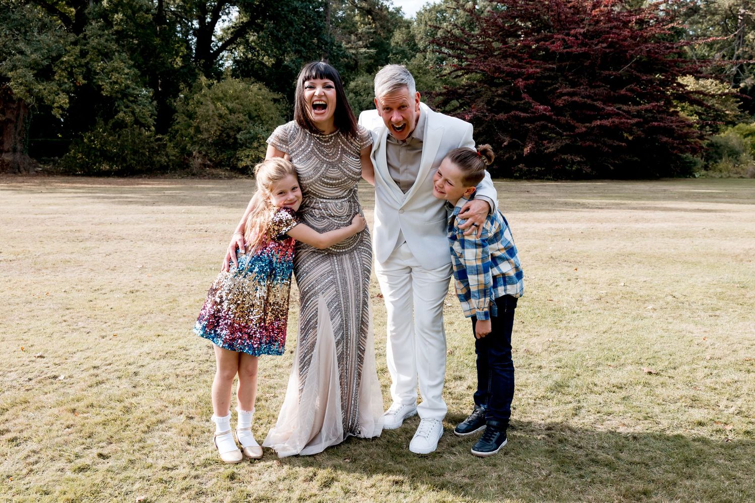 Wedding party posing for casual photos on grassy lawn during summer celebration.