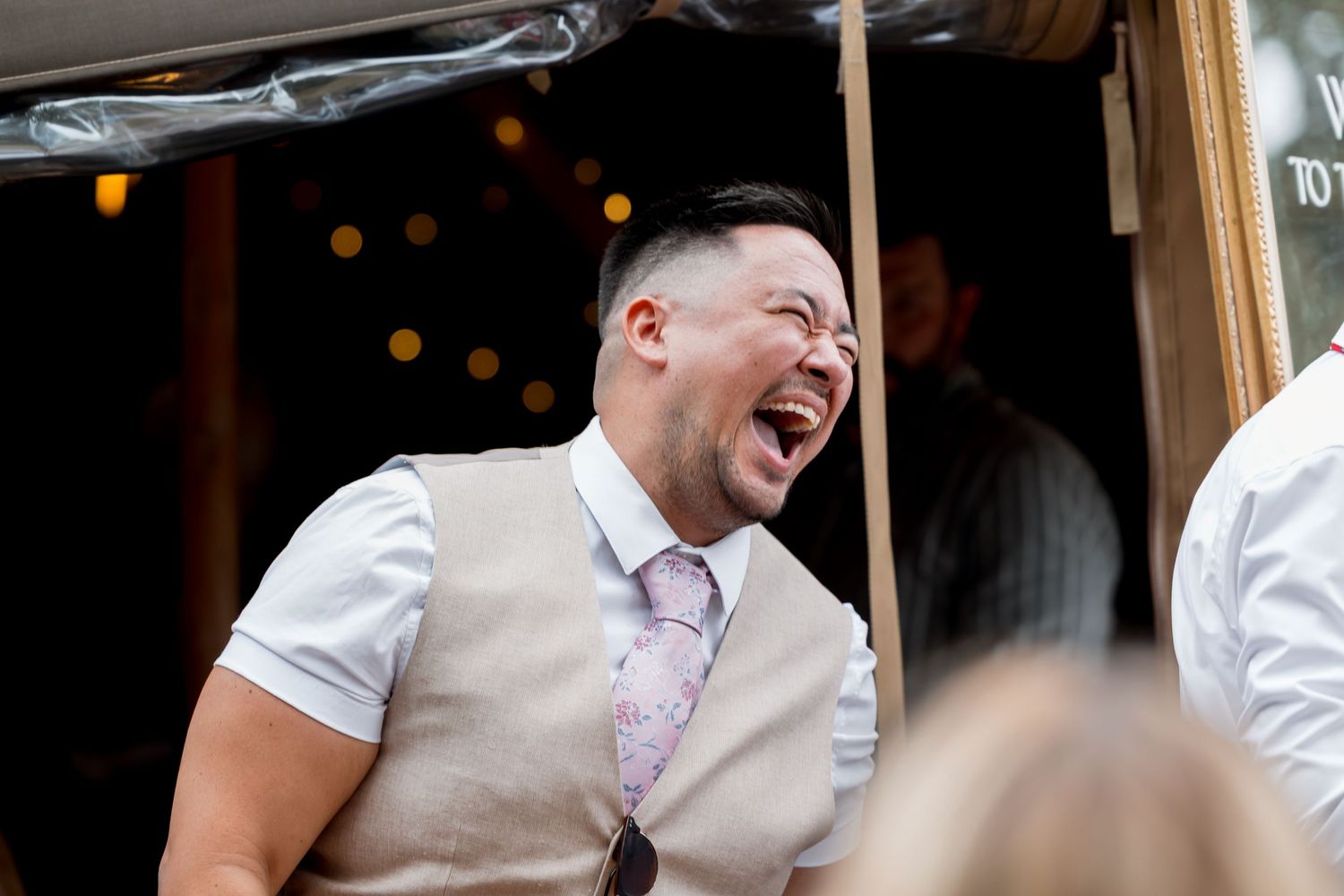 Wedding guests laugh and smile during an outdoor celebration.
