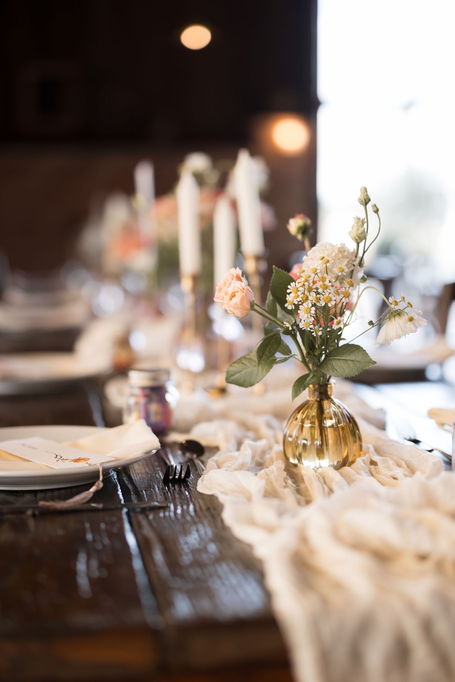 Elegant table setting with delicate floral centerpiece in gold vase and flowing fabric runner.