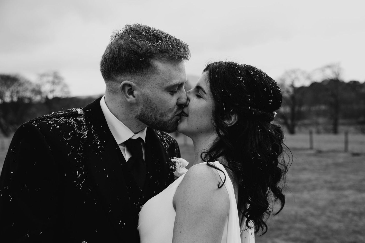 Black and white photo of newlywed couple sharing a kiss outdoors.