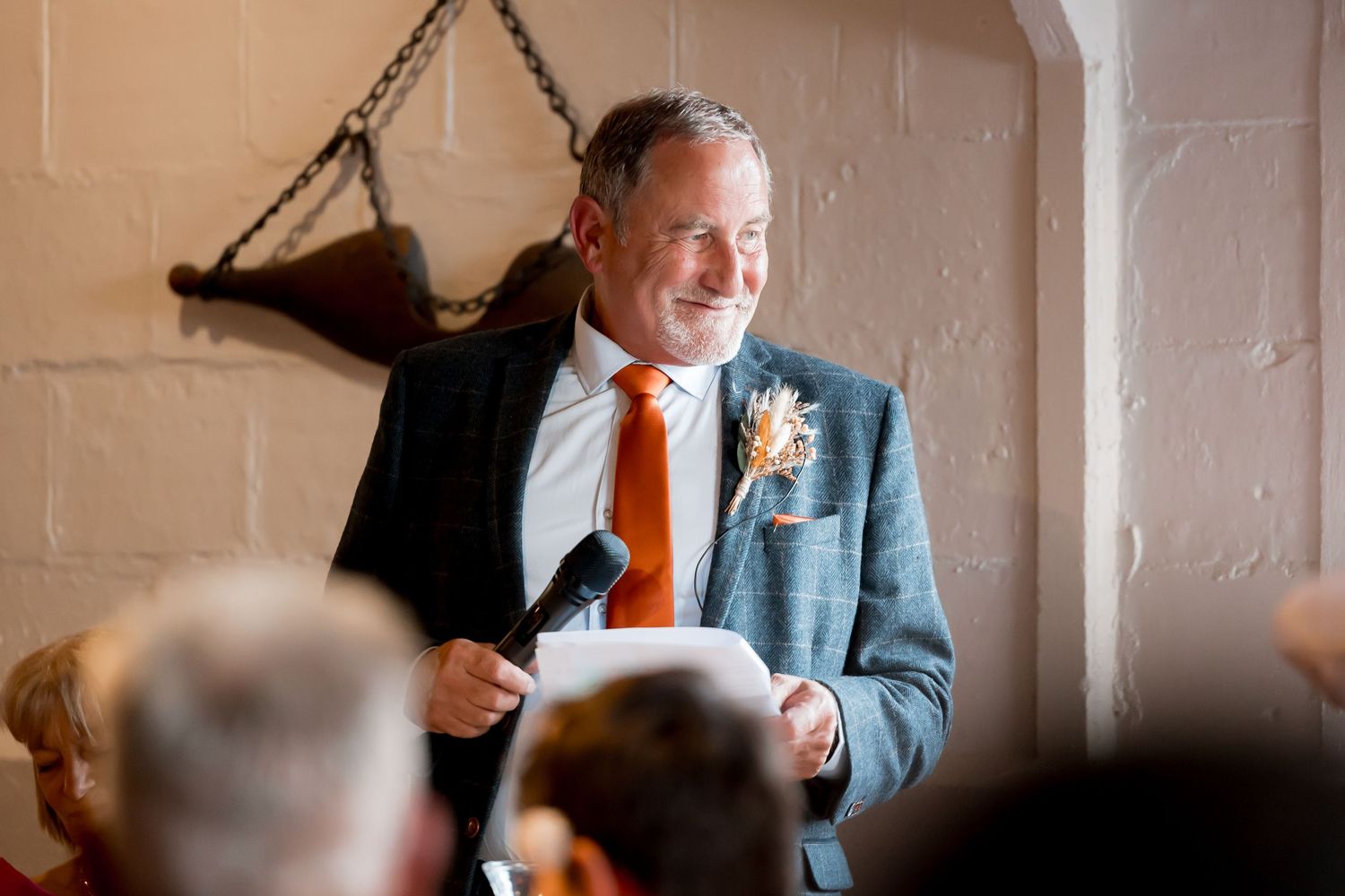 Wedding guests enjoying speeches and laughter during indoor reception.