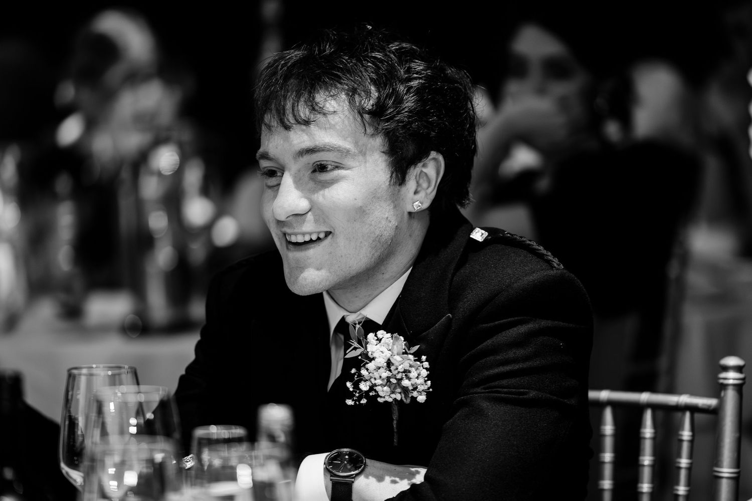 Smiling male wedding guest in black and white photo at a wedding reception dinner.