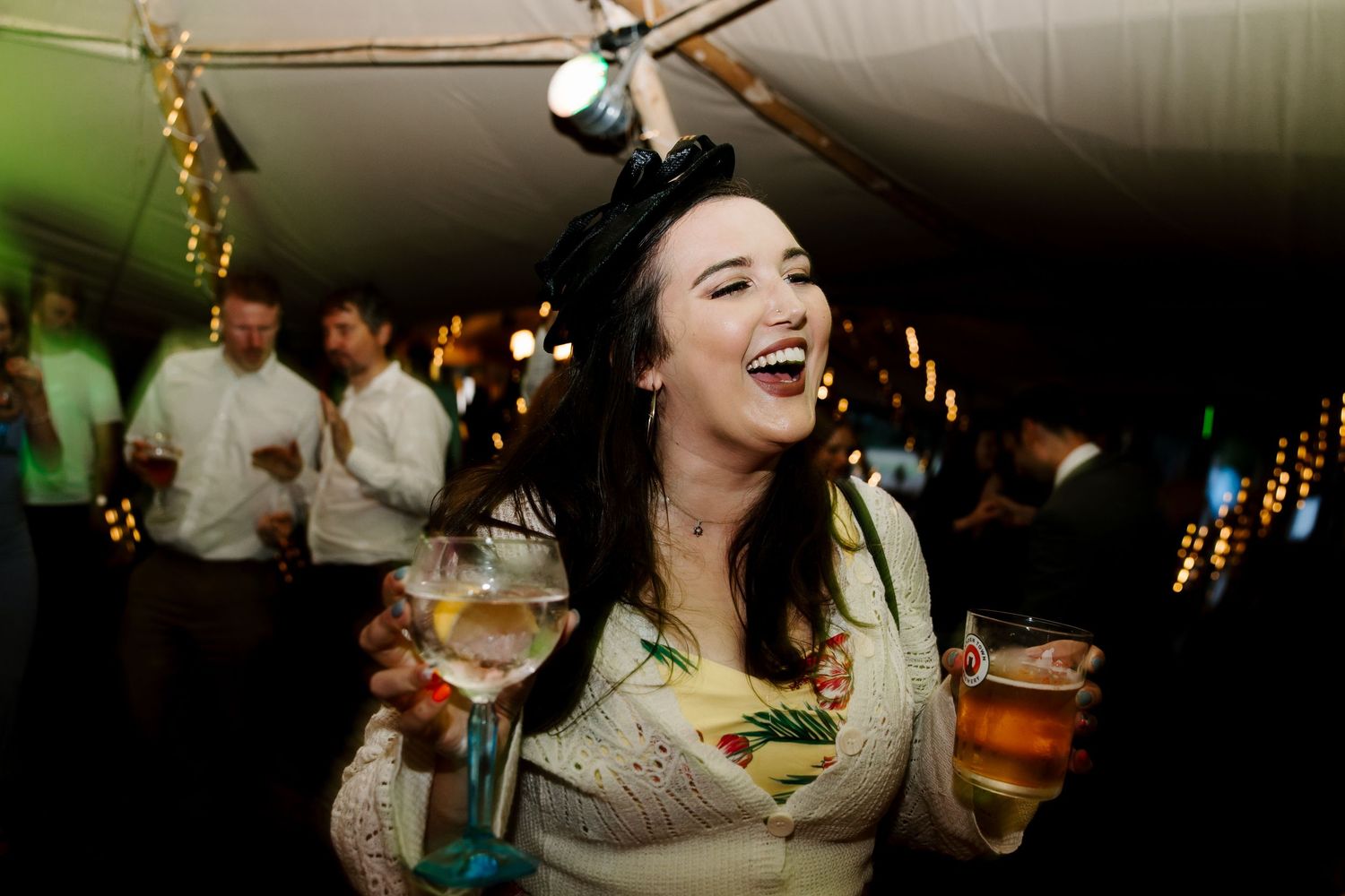 Wedding reception guests enjoying drinks and entertainment in dimly lit venue.