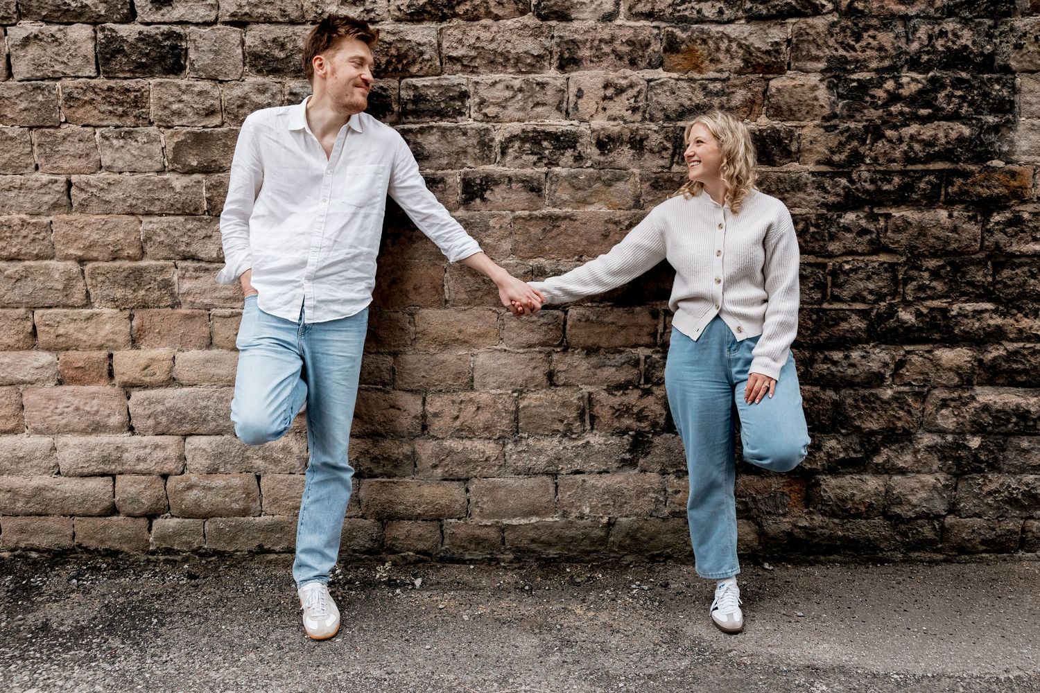 Casual engagement photos taken against a rustic brick wall background.