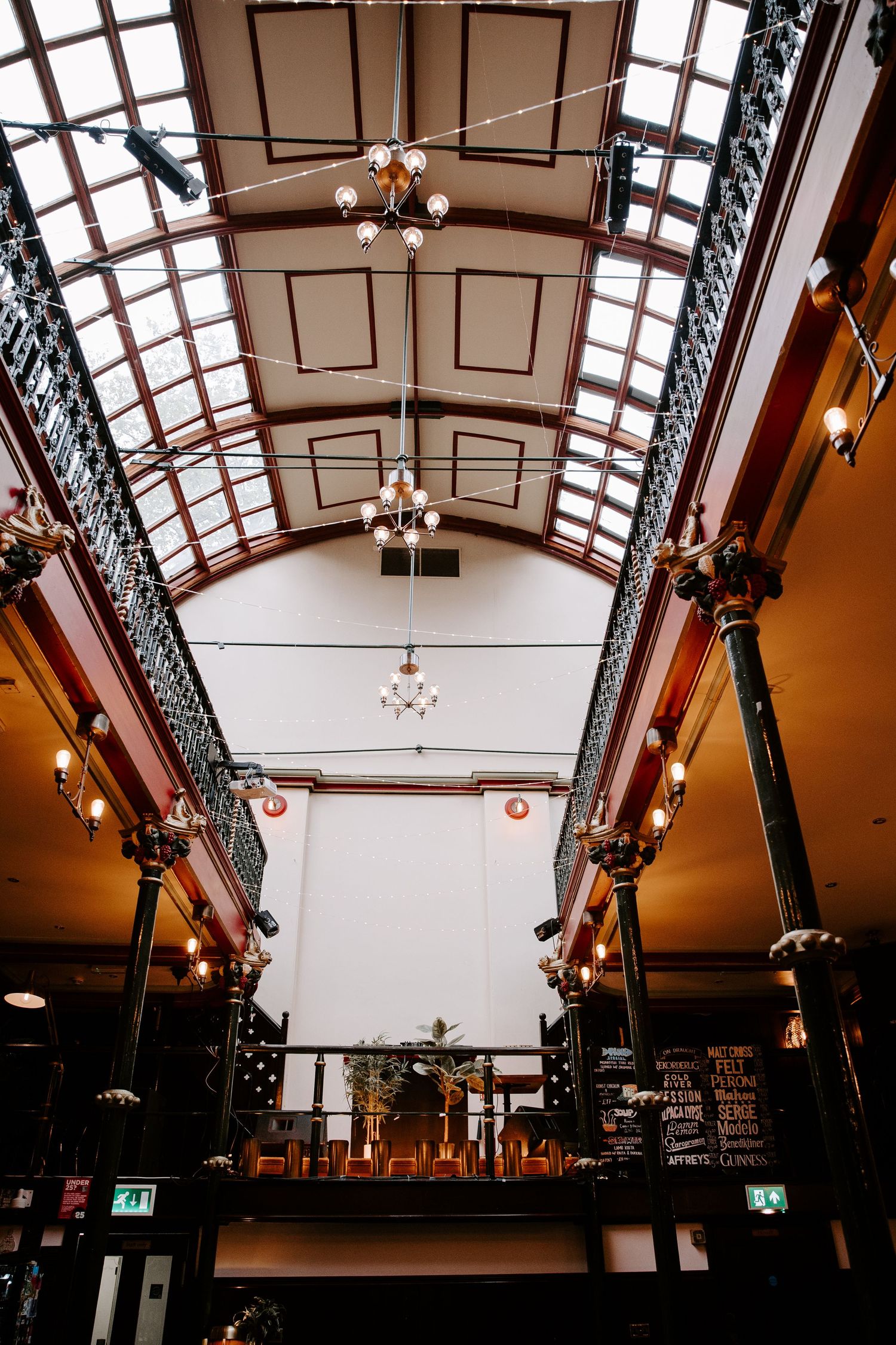Historic arcade interior with arched glass ceiling, ornate ironwork columns, chandeliers, and warm ambient lighting.