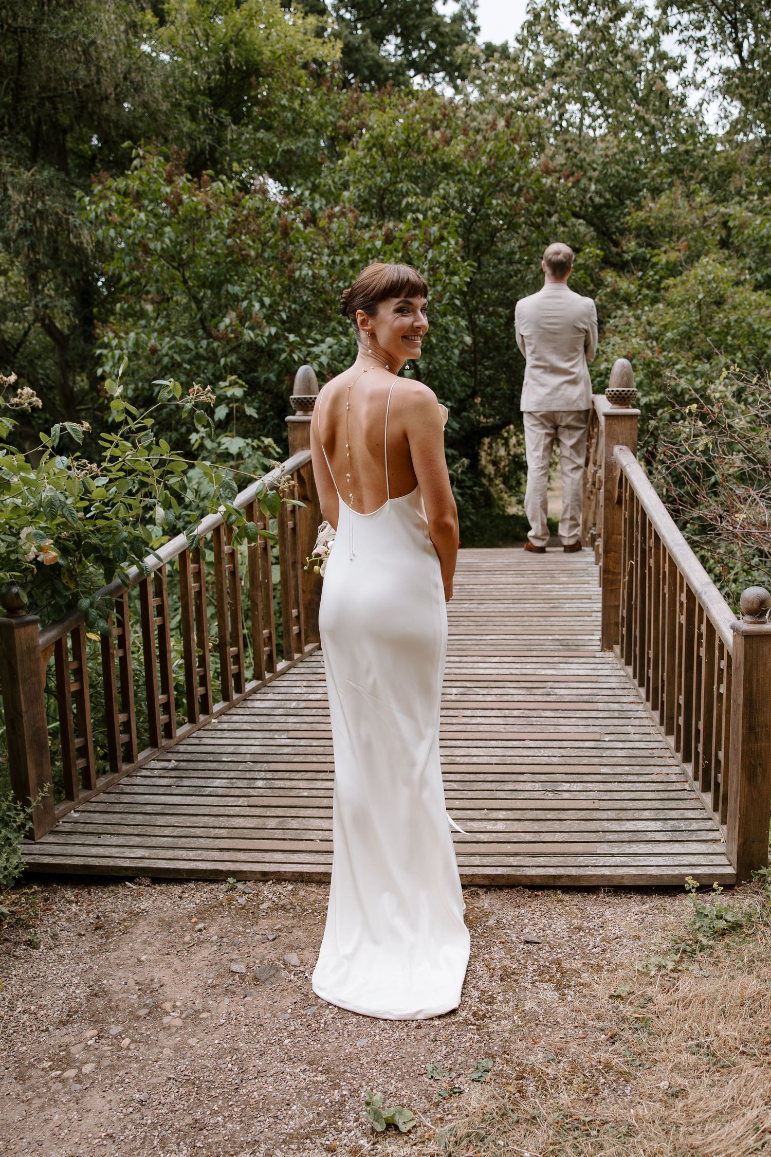 Wedding party walking across wooden bridge in outdoor garden setting.