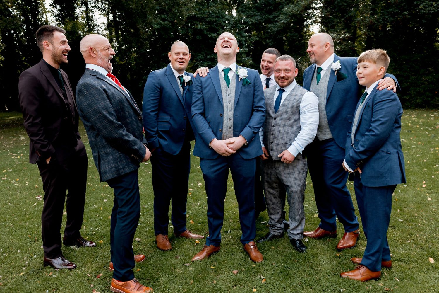 A group of groomsmen in navy suits gather outdoors for a casual portrait.