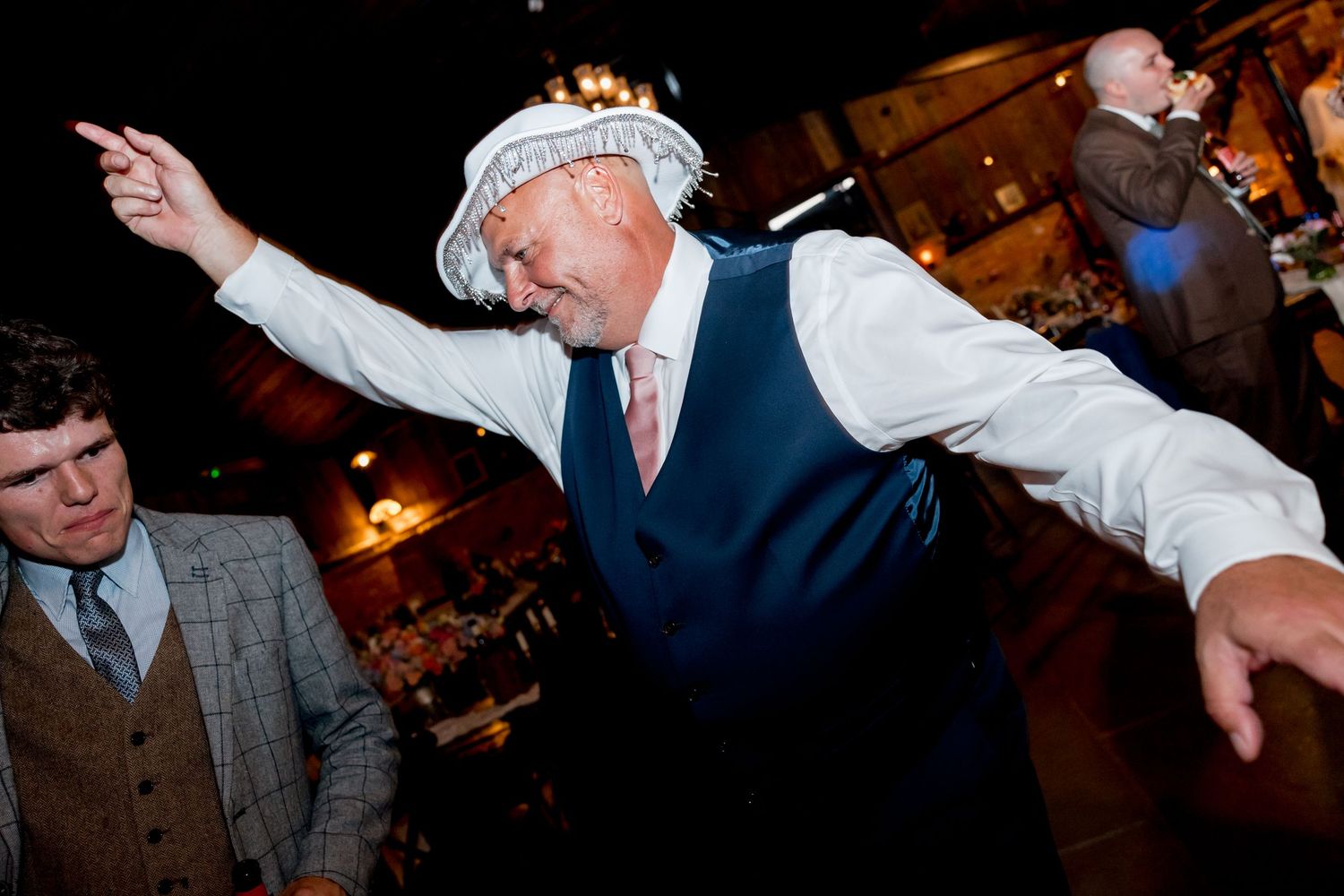 Guest in vest and tie dancing with arms spread wide at wedding reception.