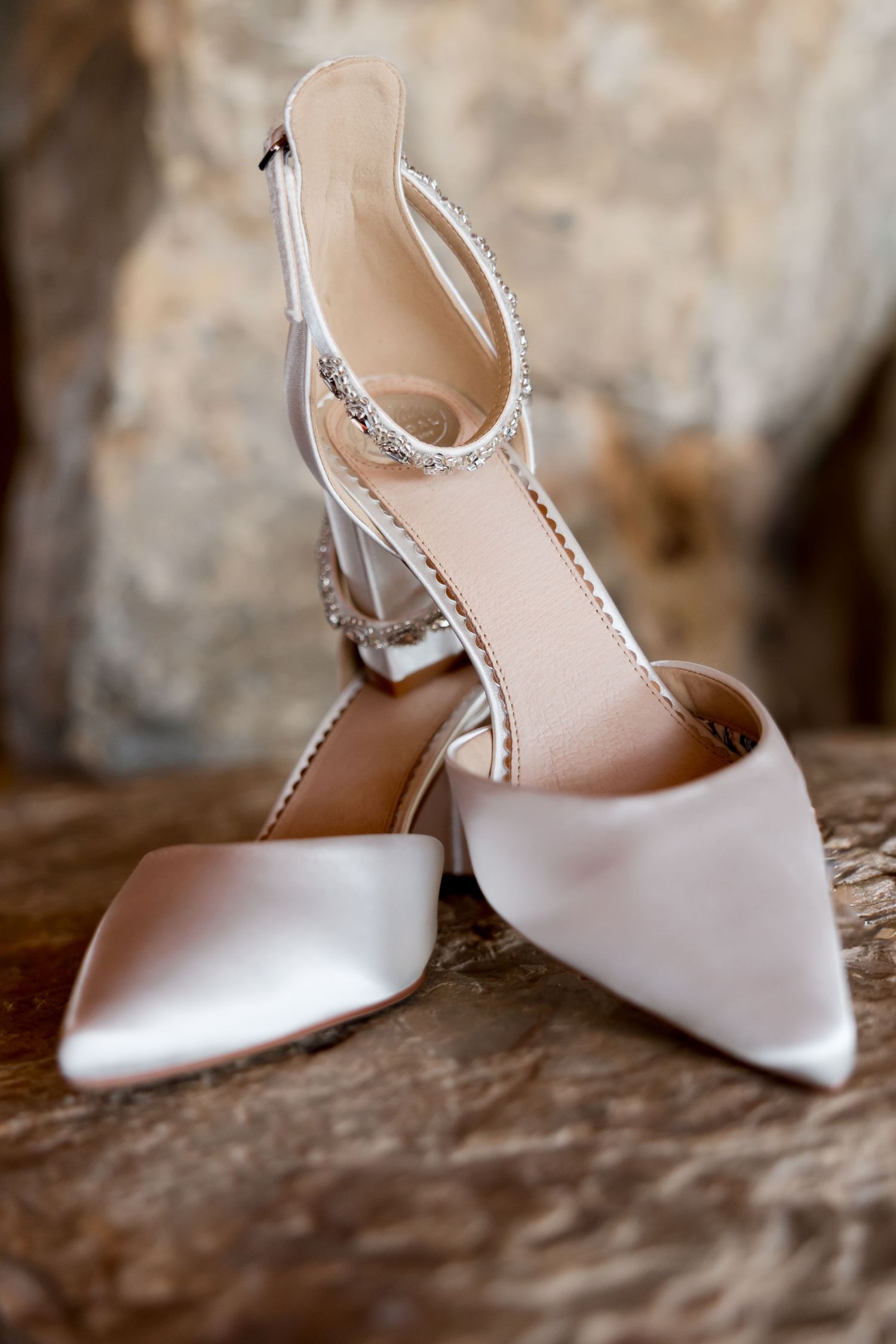 Elegant white bridal shoes with delicate details photographed on a stone surface.