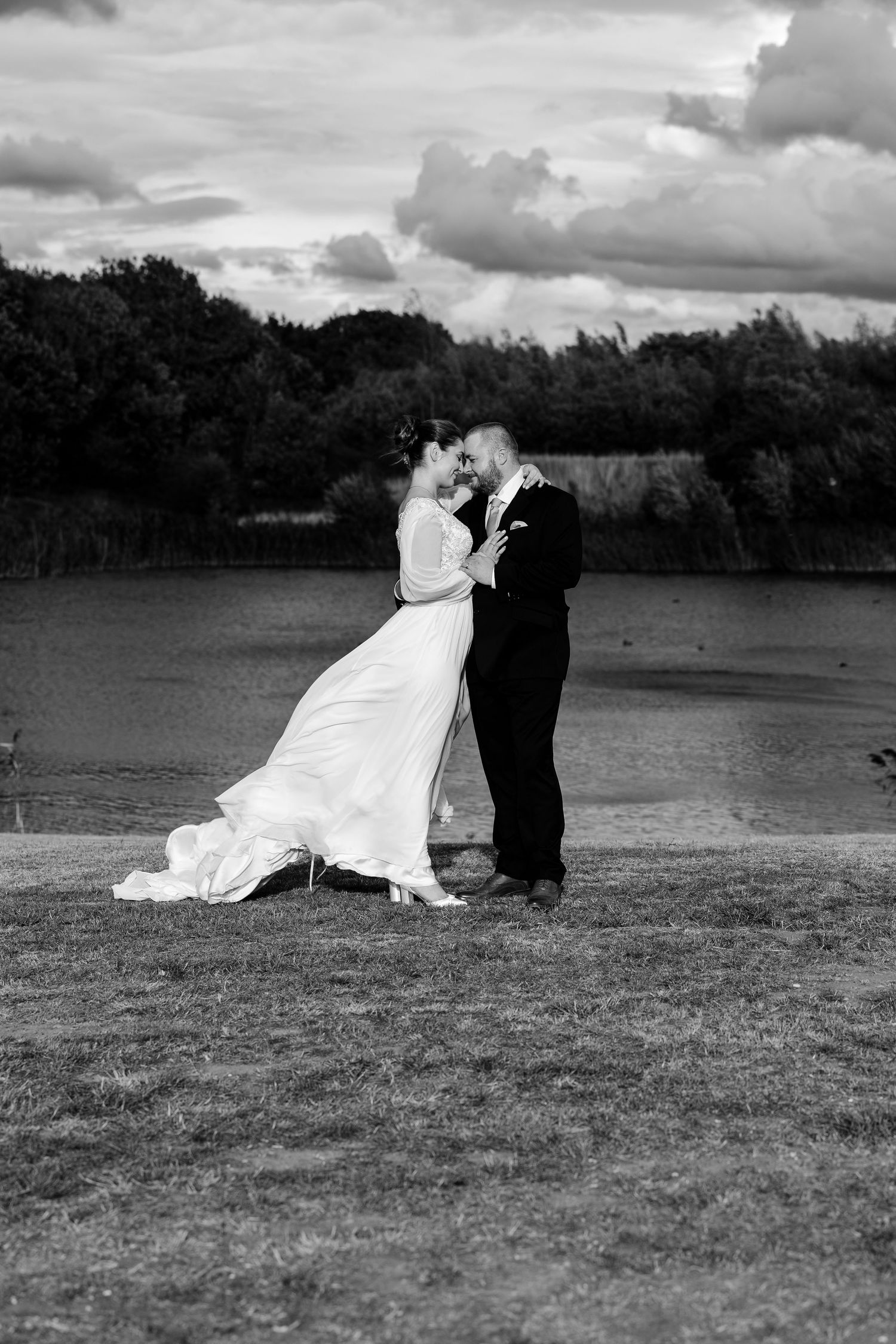 A black and white wedding photo captures a romantic moment in a scenic field.