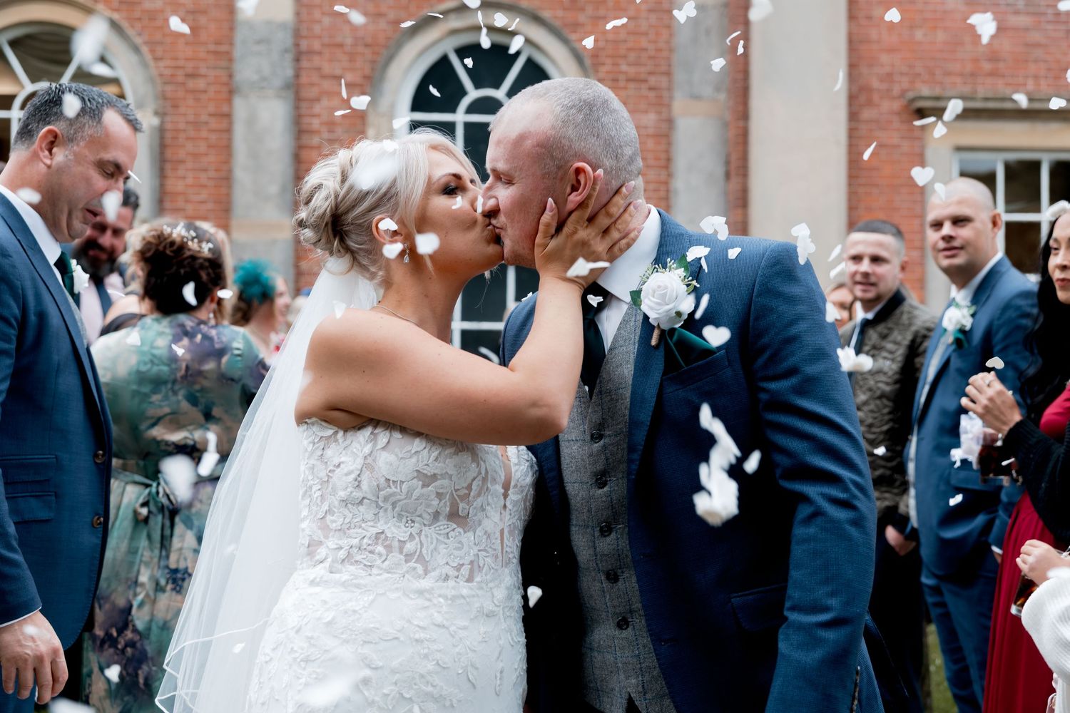 Wedding celebration with guests throwing confetti outside a brick building.