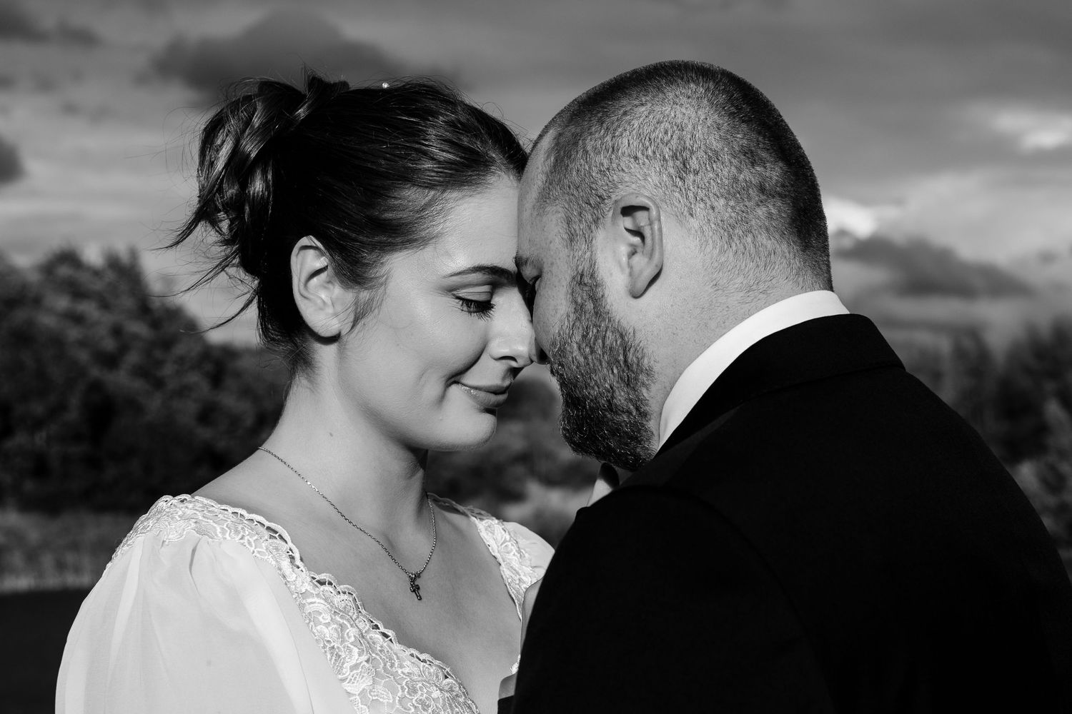 Intimate black and white portrait of a couple sharing a romantic moment against a dramatic sky.